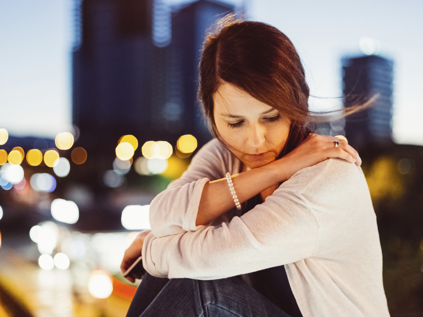 Sad woman sitting thoughtfully against the cityscape