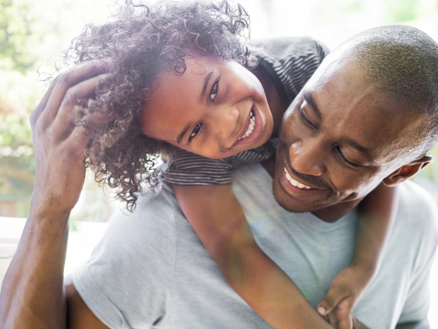 A photo of happy girl with arms around father. Young man is looking at daughter smiling. They are in casuals at home.