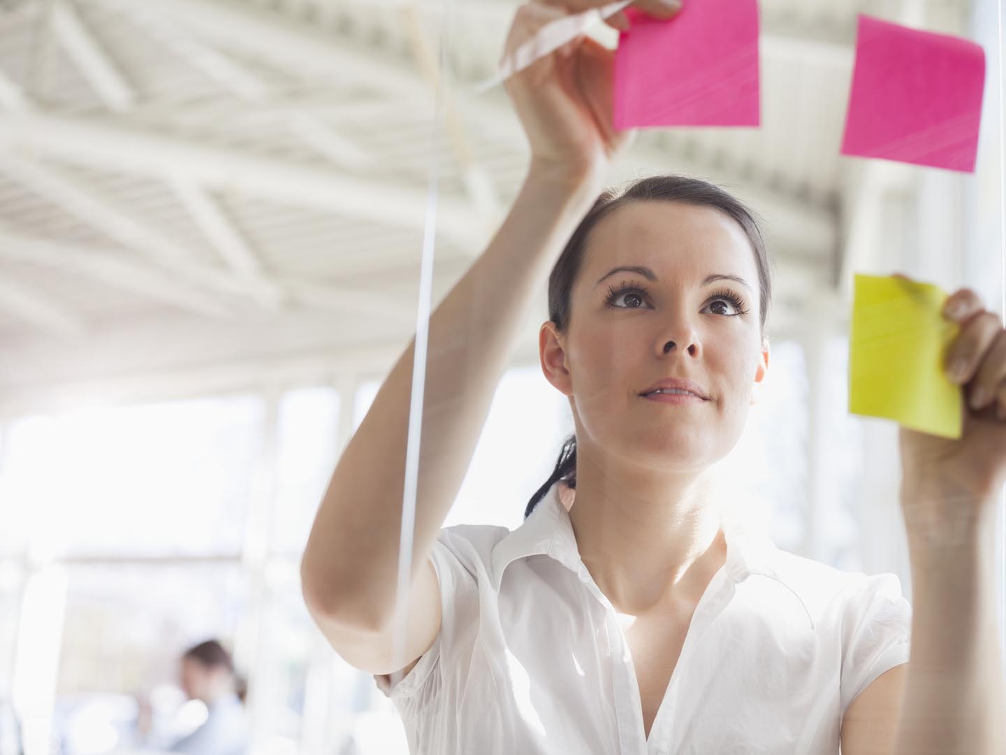 Beautiful young businesswoman putting adhesive notes on glass wall in office