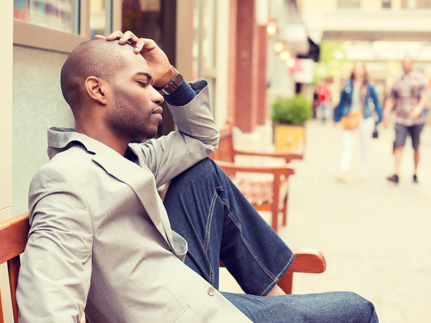 side profile stressed young casual businessman sitting outside corporate office holding head with hands looking down. Negative human emotion facial expression feelings.