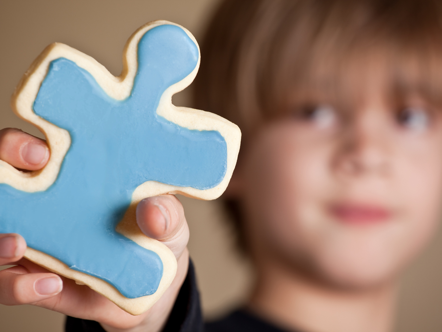"A 9 year old boy holding out a blue iced puzzle piece shaped sugar cookie. Shallow DOF, focus on cookie only.April is Autism Awareness month. Colorful puzzle pieces are often used to represent Autism awareness. 1 in 88 children in the USA are diagnosed with an ASD (Autism Spectrum Disorder)."