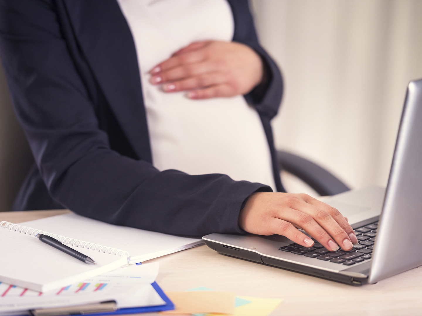 A pregnant woman hand on belly closeup uses laptop in the office