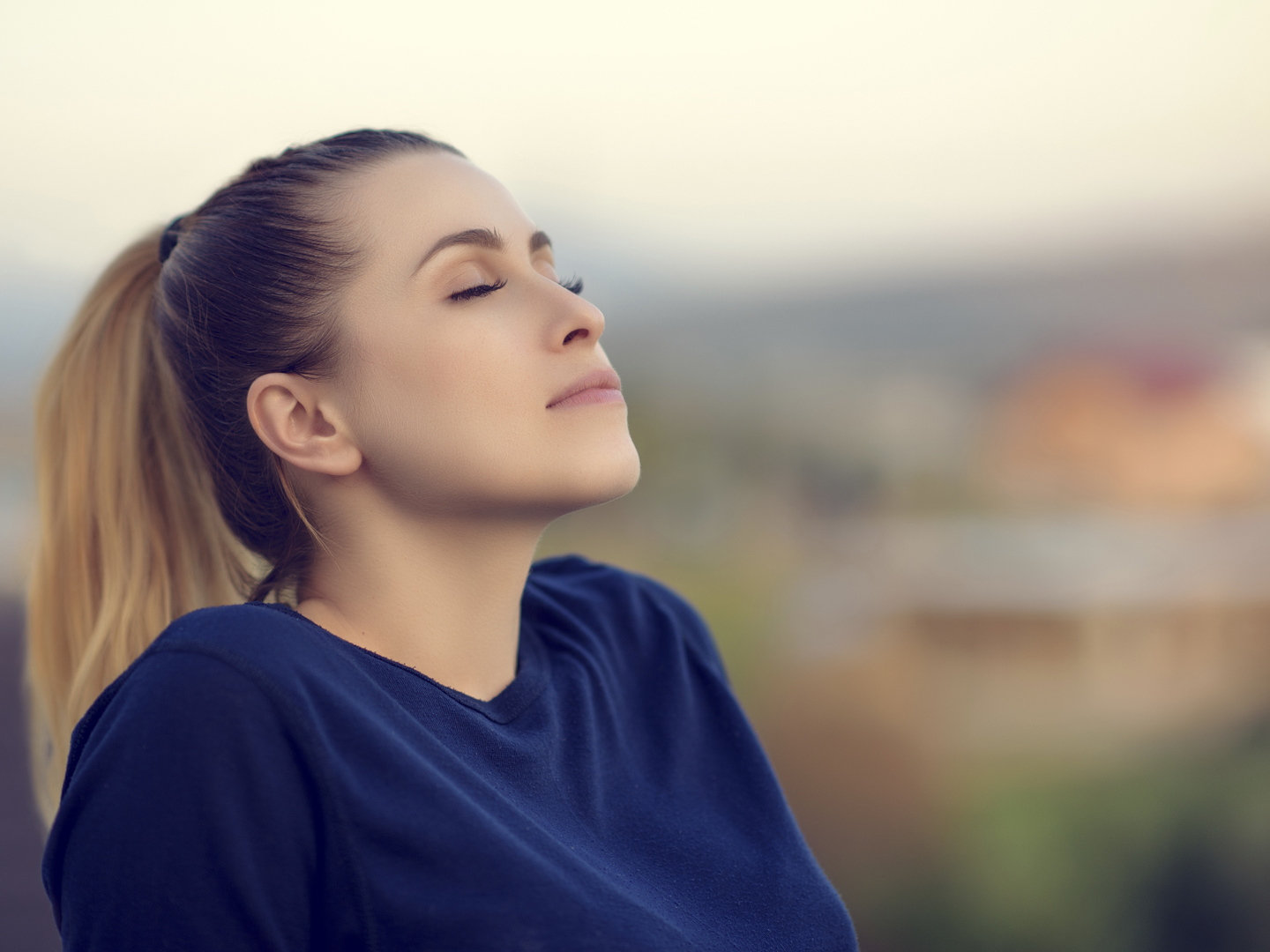 joyful and relaxed young woman with her eyes closed enjoying her time outdoors.side view, sunset time.