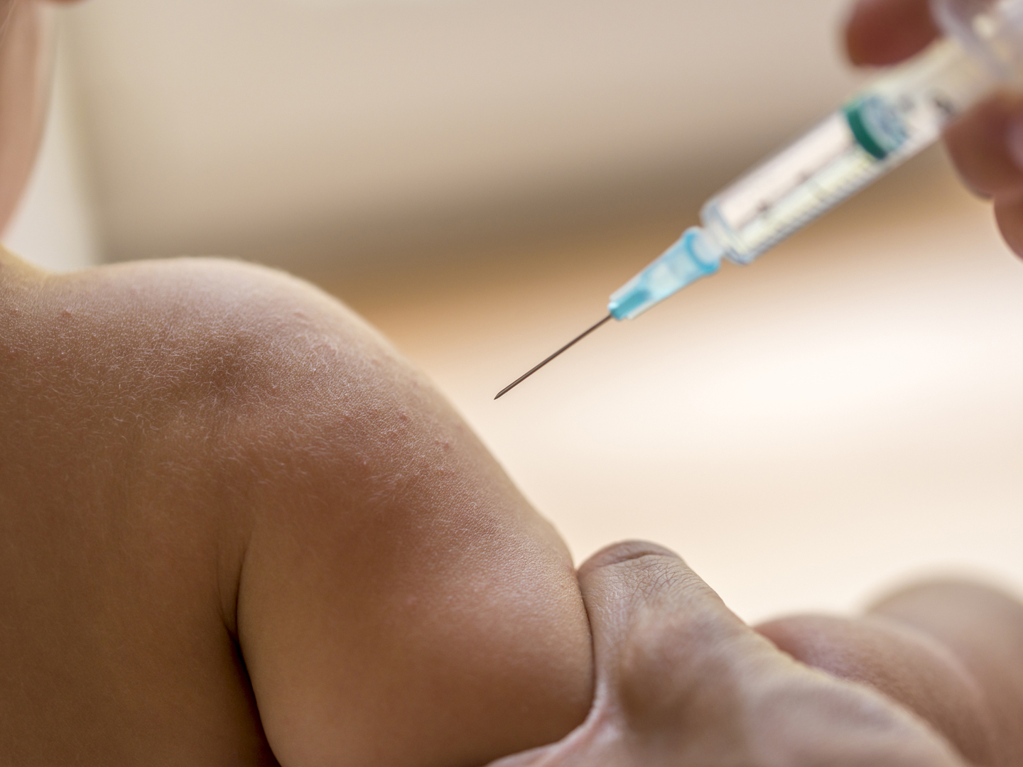 Doctor injecting a young child with a vaccination or antibiotic in a small disposable hypodermic syringe, close up of the kids arm and needle.