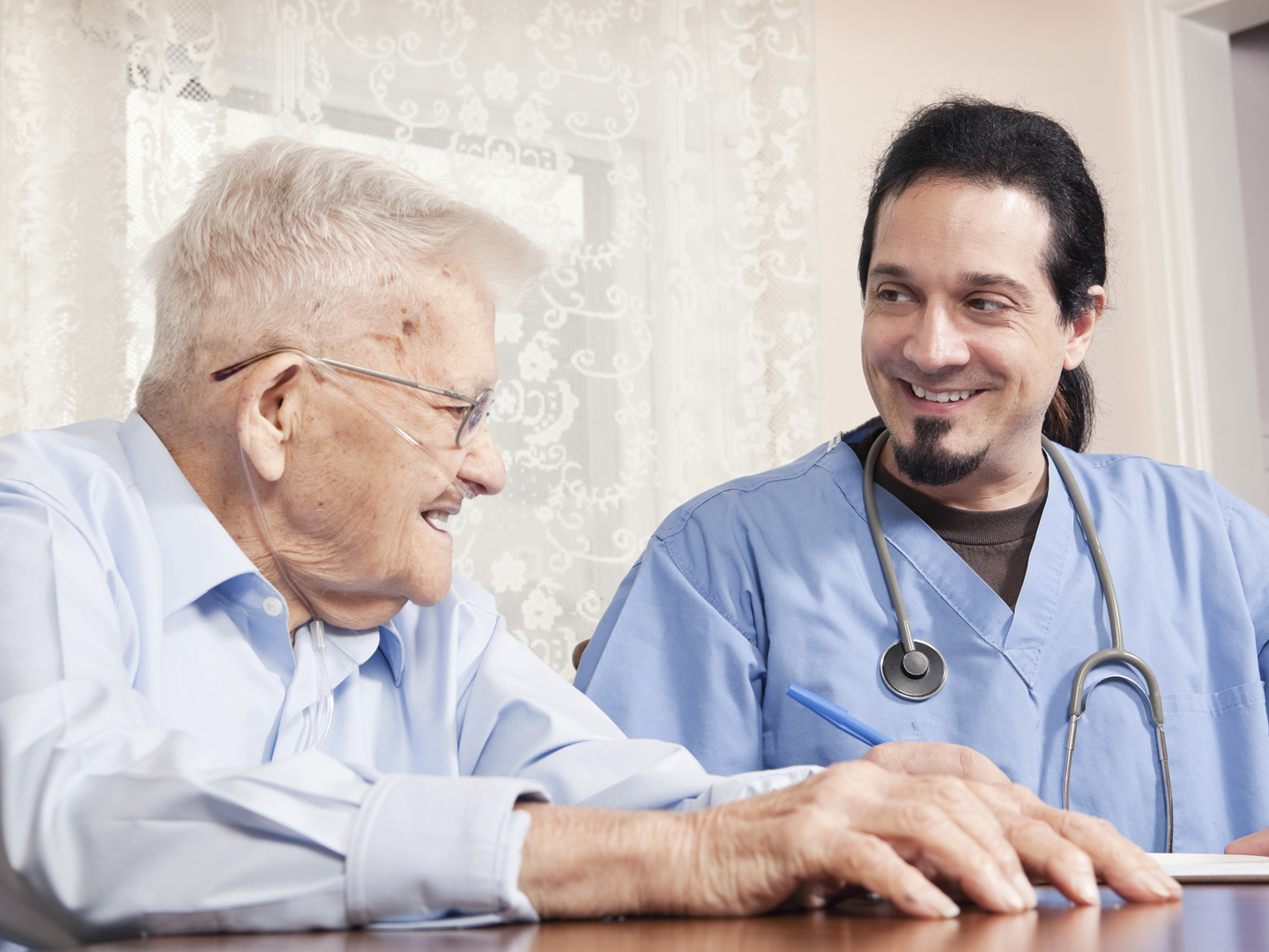 An in home healthcare nurse smiling with his 90 year old patient as they go over his chart.