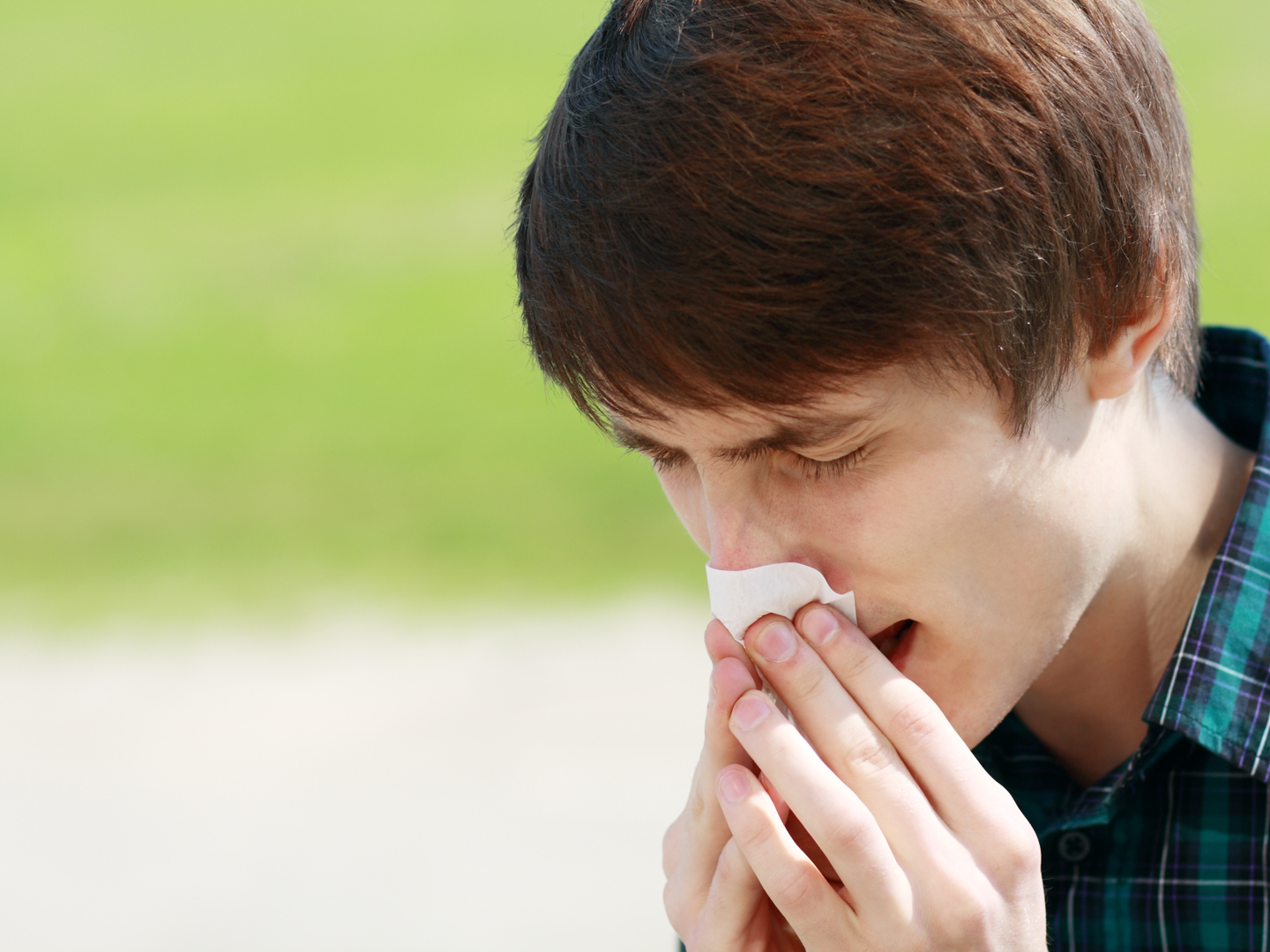 Young man sneezing outdoor and blowing his nose because he has allergies.
