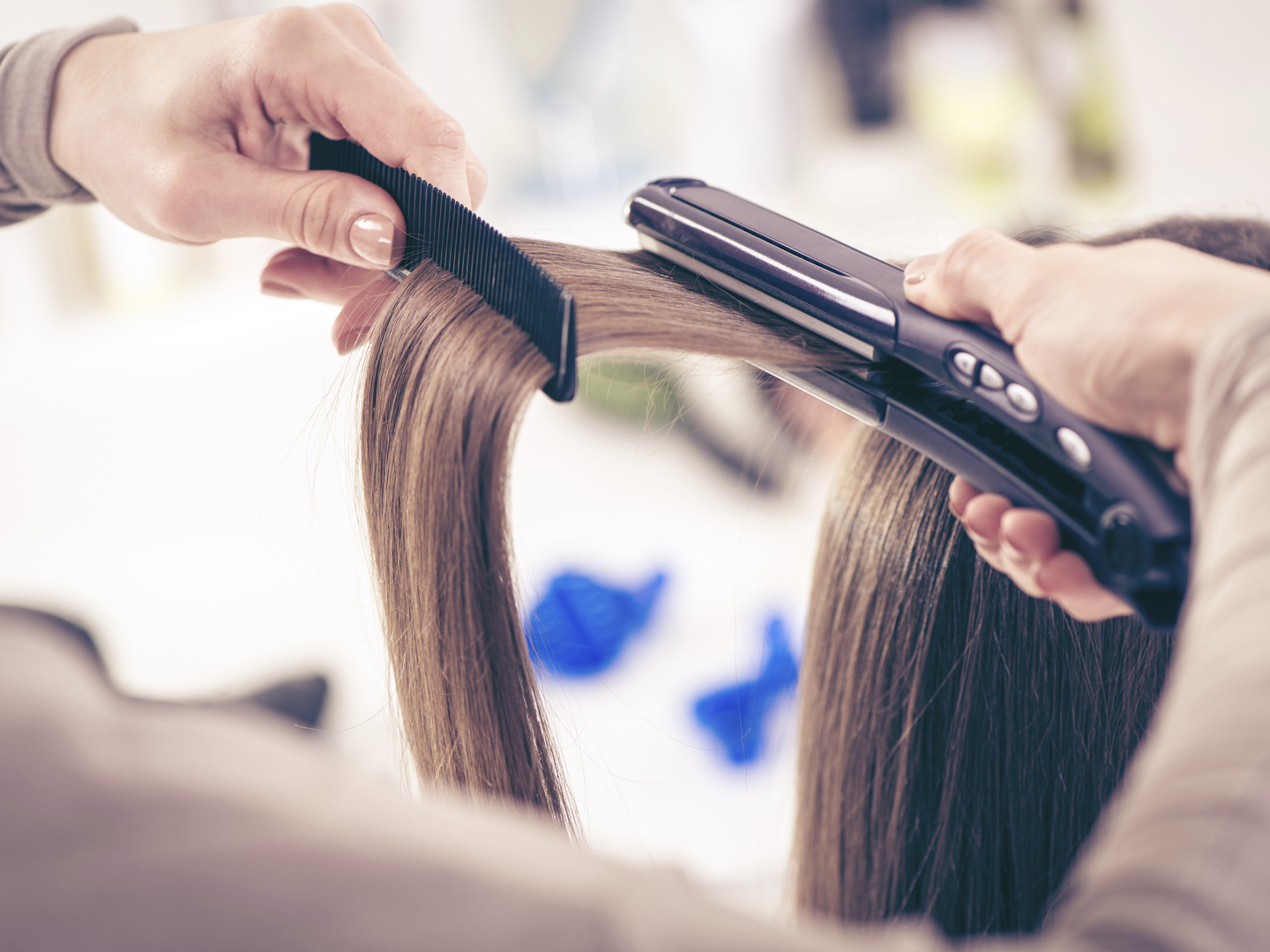 Close-up of a hairdresser straightening long brown hair with hair irons.