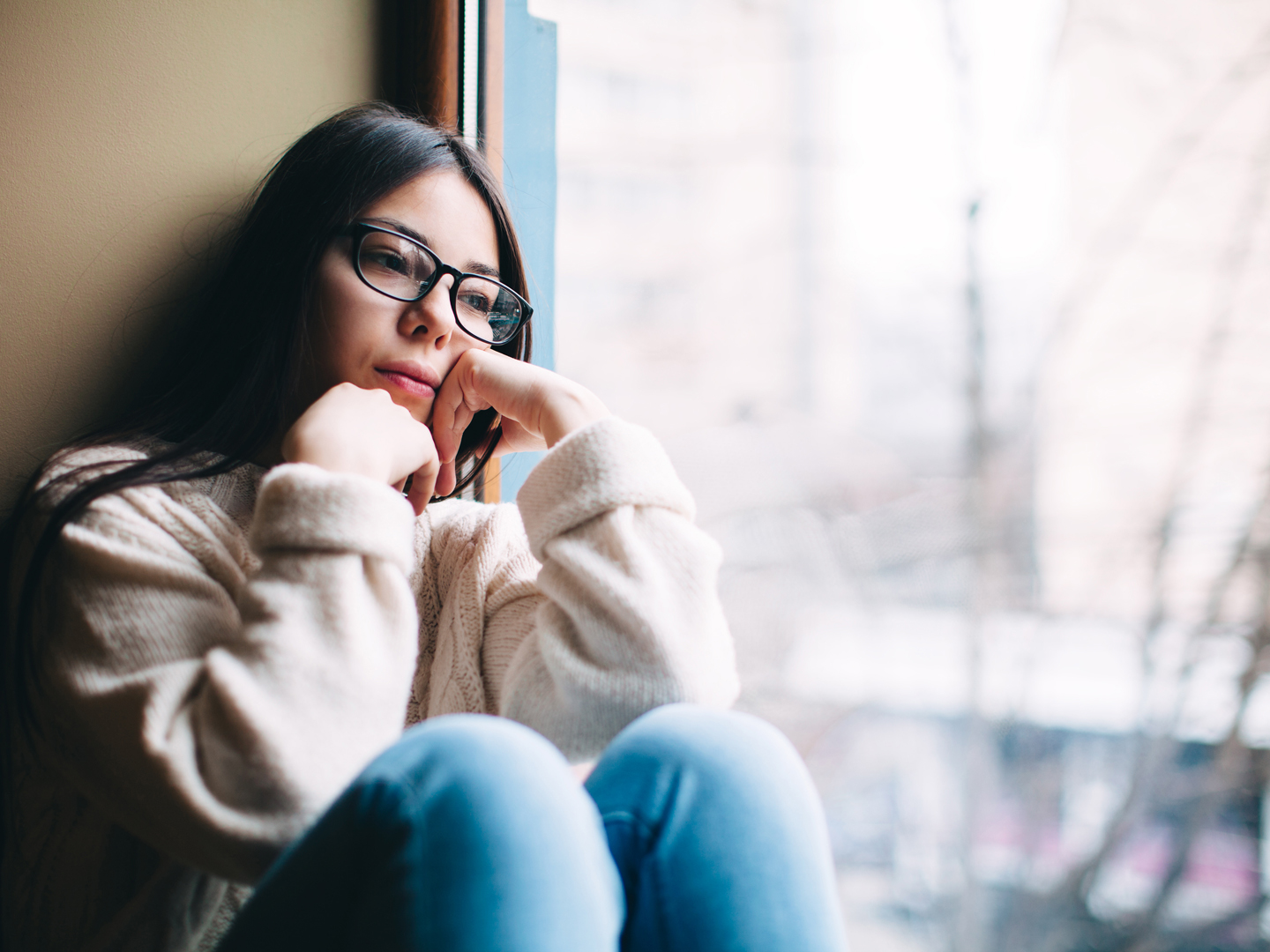 Sad teenage girl looking out the window on a cold autumn day