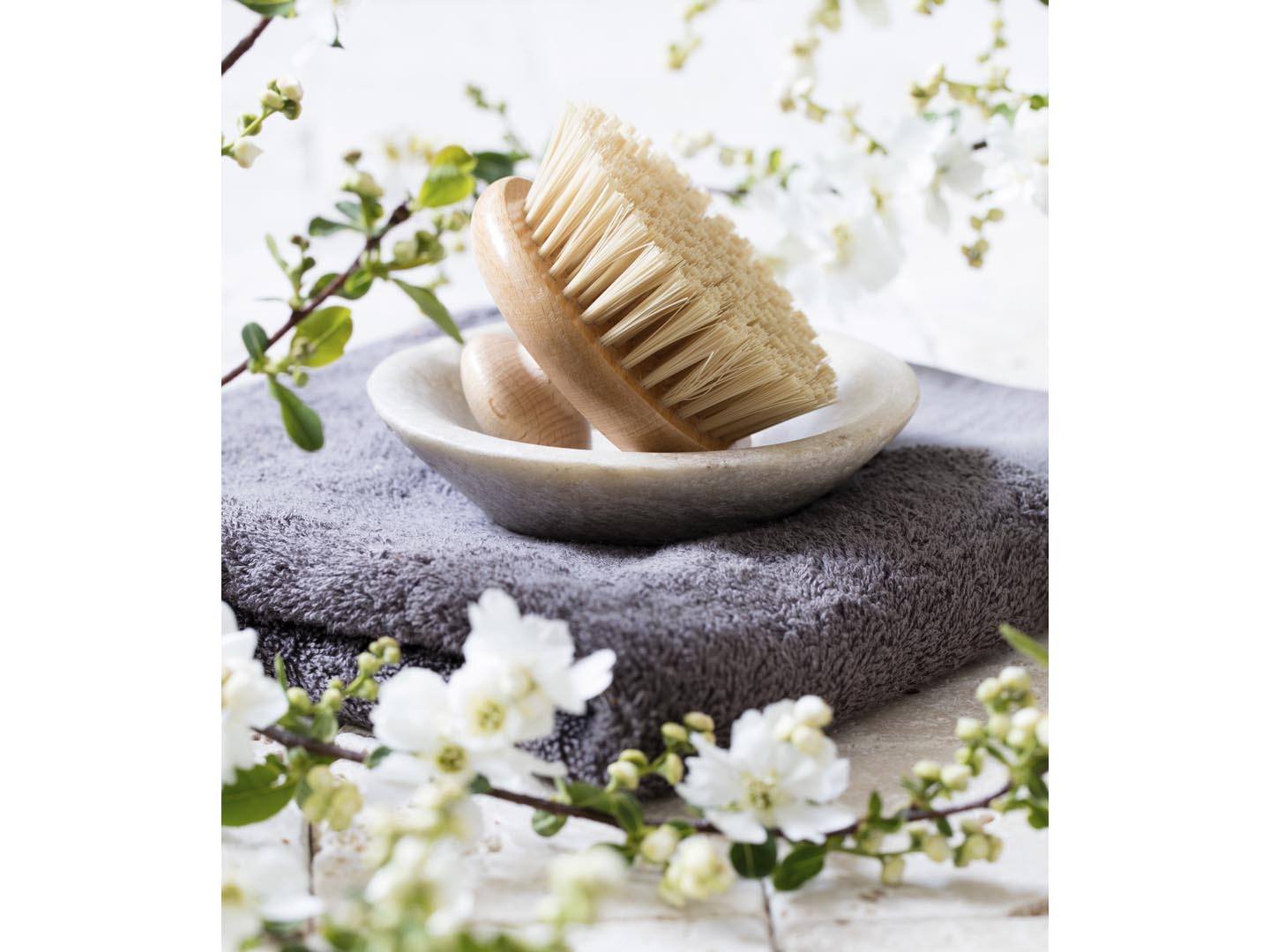 detox still-life - body brush in mineral cup holder over towel and fresh white spring blossom flowers for natural beauty and washing up routine