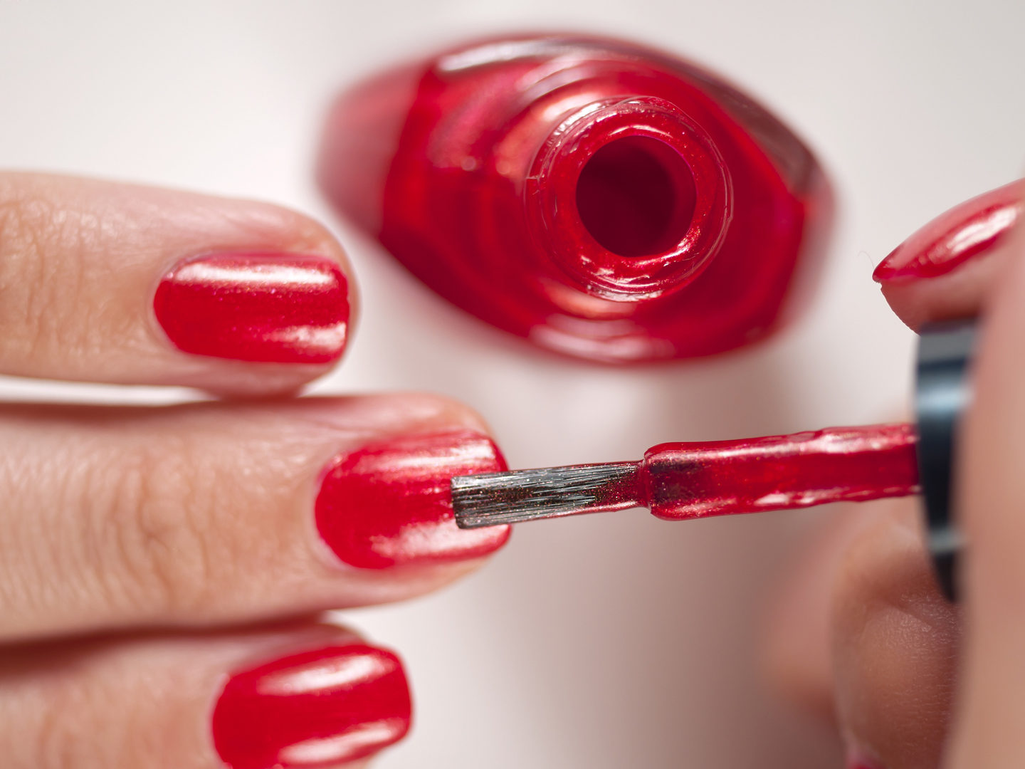 Manicurist applying red nail polish on female fingers