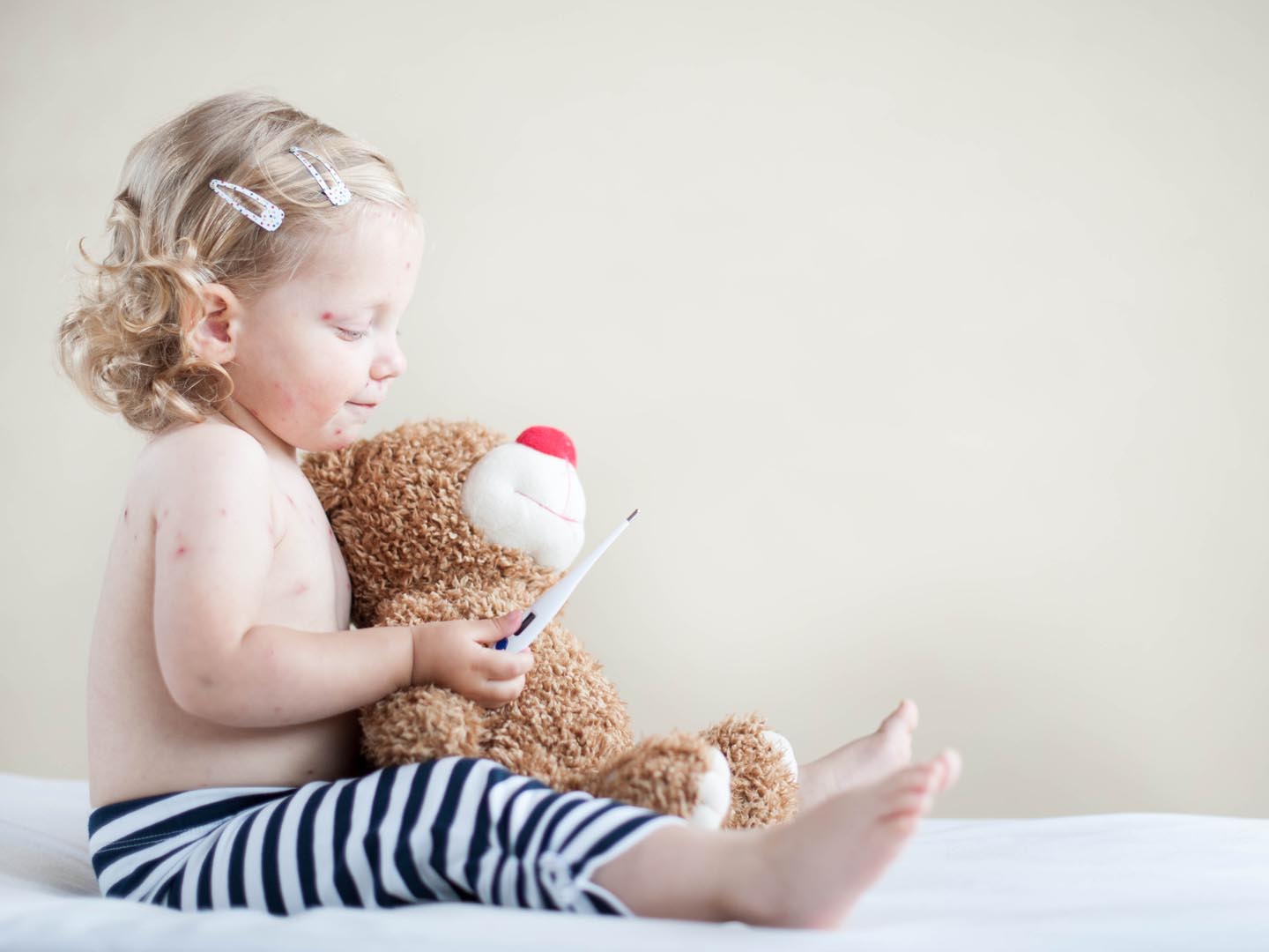 Sick girl is sitting on the bed with teddy-bear