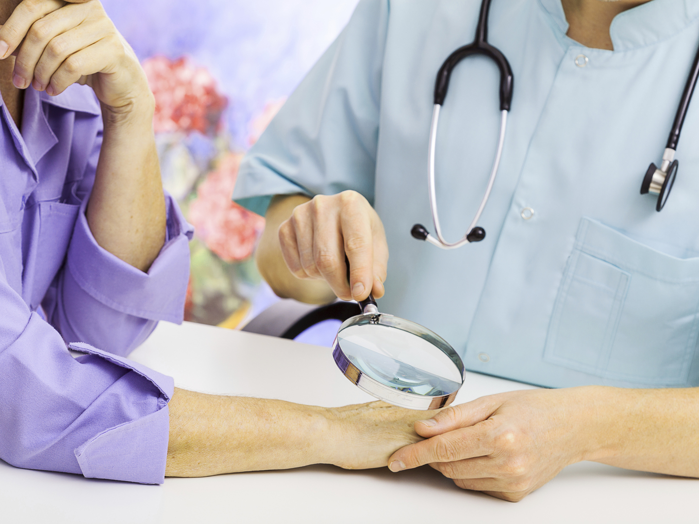 Dermatologist looking at woman&#039;s hand through a magnifying glass