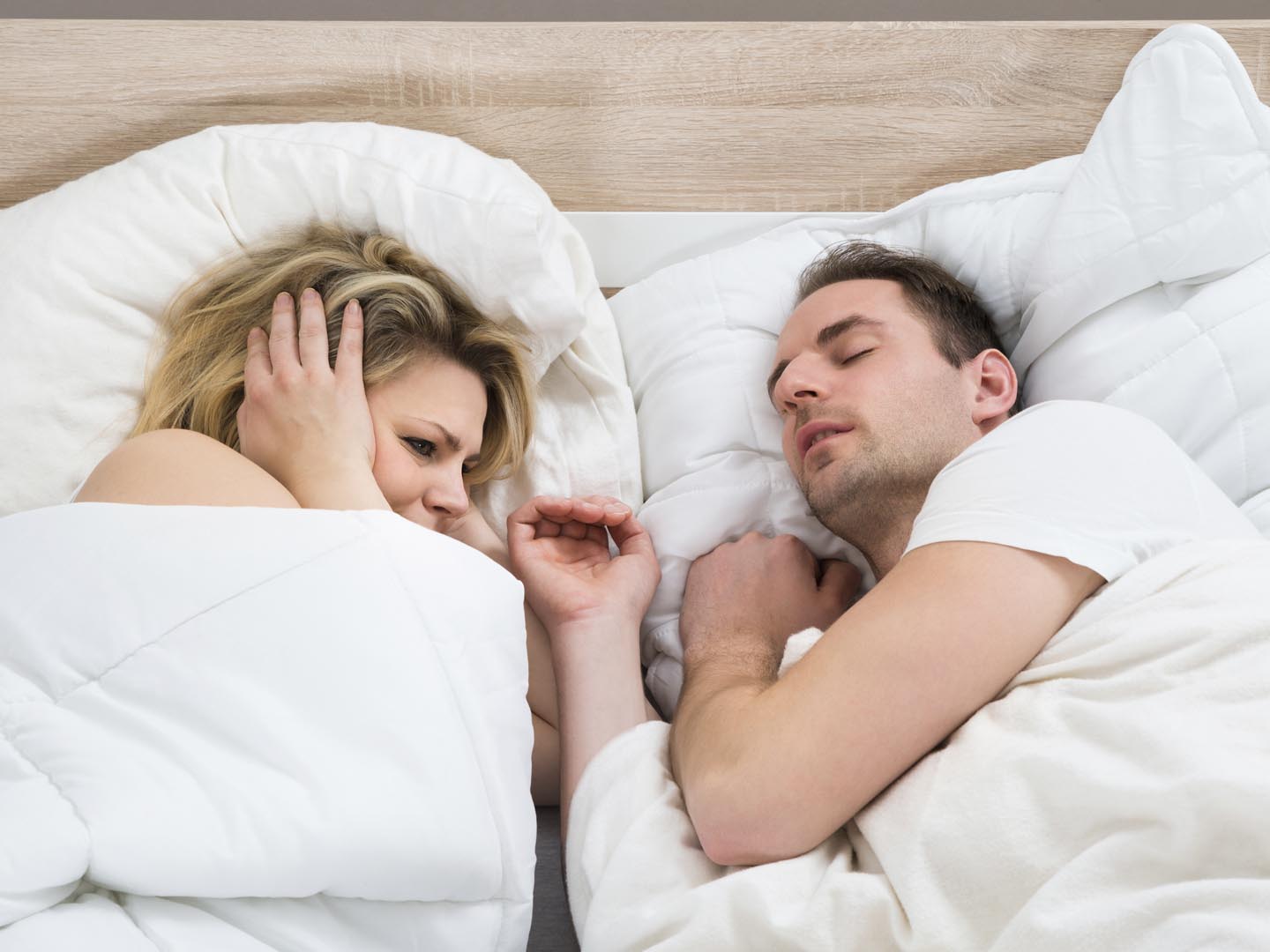 Woman Covering Ears While Man Snoring In Bed At Home
