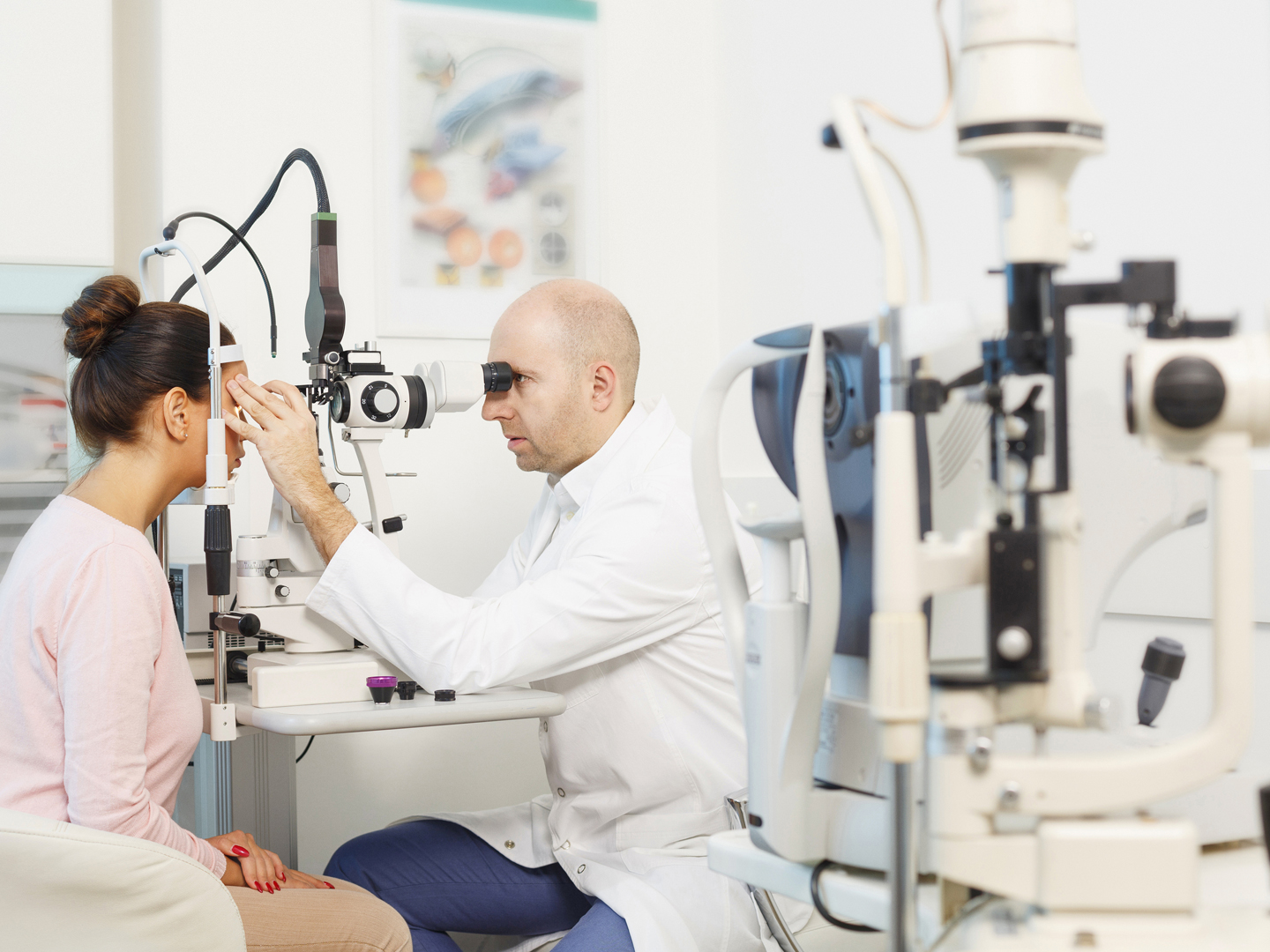 Ophthalmology - ophthalmic clinic. Doctor ophthalmologist  optometrist,  medical eye examination.  Young women, patient  having a checkup, eye examined by specialist.  Very shallow depth of field for soft background. Professional make-up, hairstyle and retouch. Shot with Canon 5DMarkIII, developed from RAW, Adobe RGB color profile.