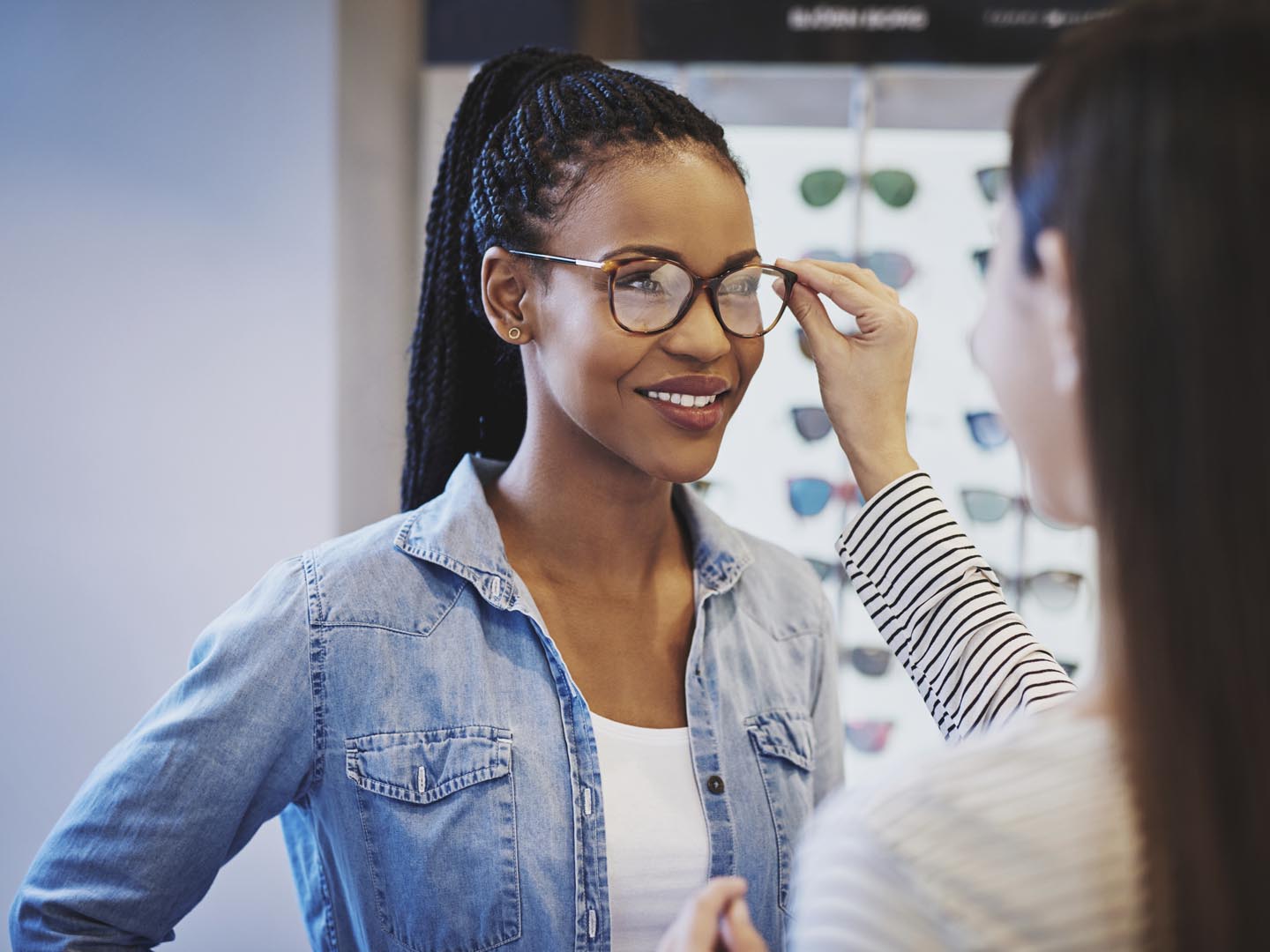 Optometrist fitting glasses on an attractive African American woman customer inside a store as she selects a frame