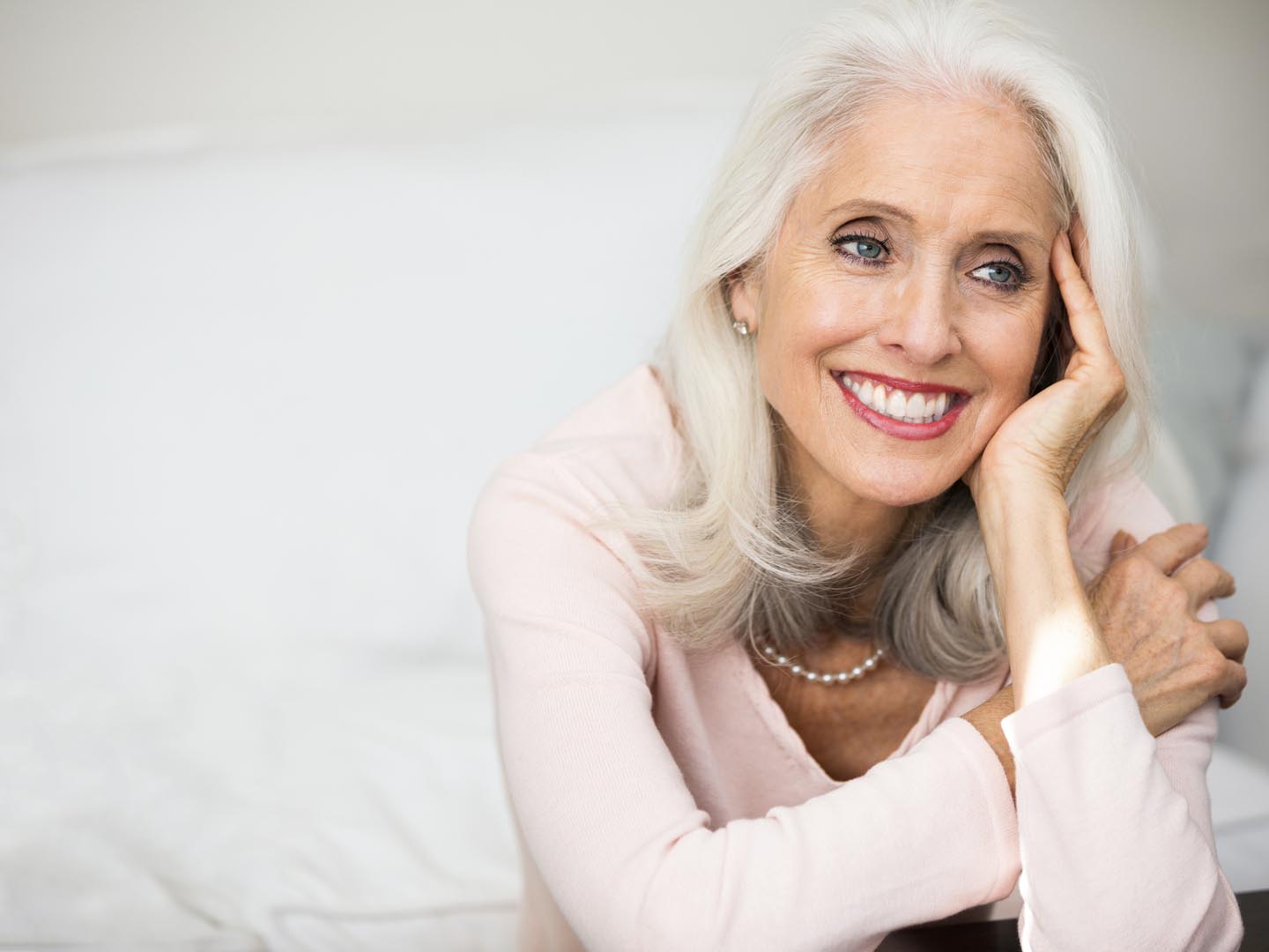 Portrait of a woman in her golden age. Portrait of a beautiful woman in her 60s. She is mature, confident and happy. Woman has grey hair. Woman is Caucasian with blue eyes and beautiful smile. She is leaning her head on her wrist.