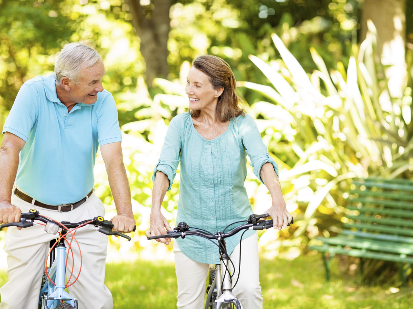 Happy senior couple looking at each other while sitting on bicycles in park. Horizontal shot.