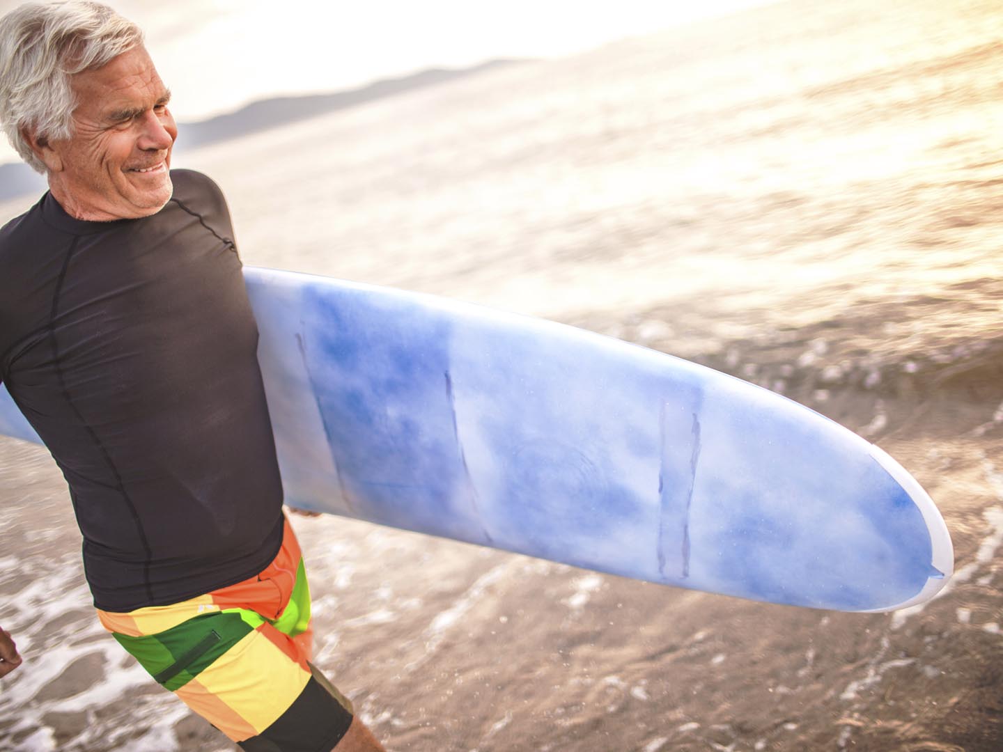 Portrait of a senior surfer holding his surfboard, being satisfied after a good surfing day