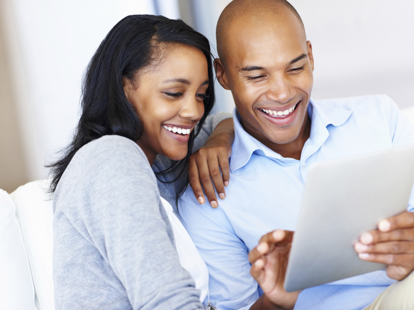 Laughing African-American couple using a digital tablet from the comfort of their lounge