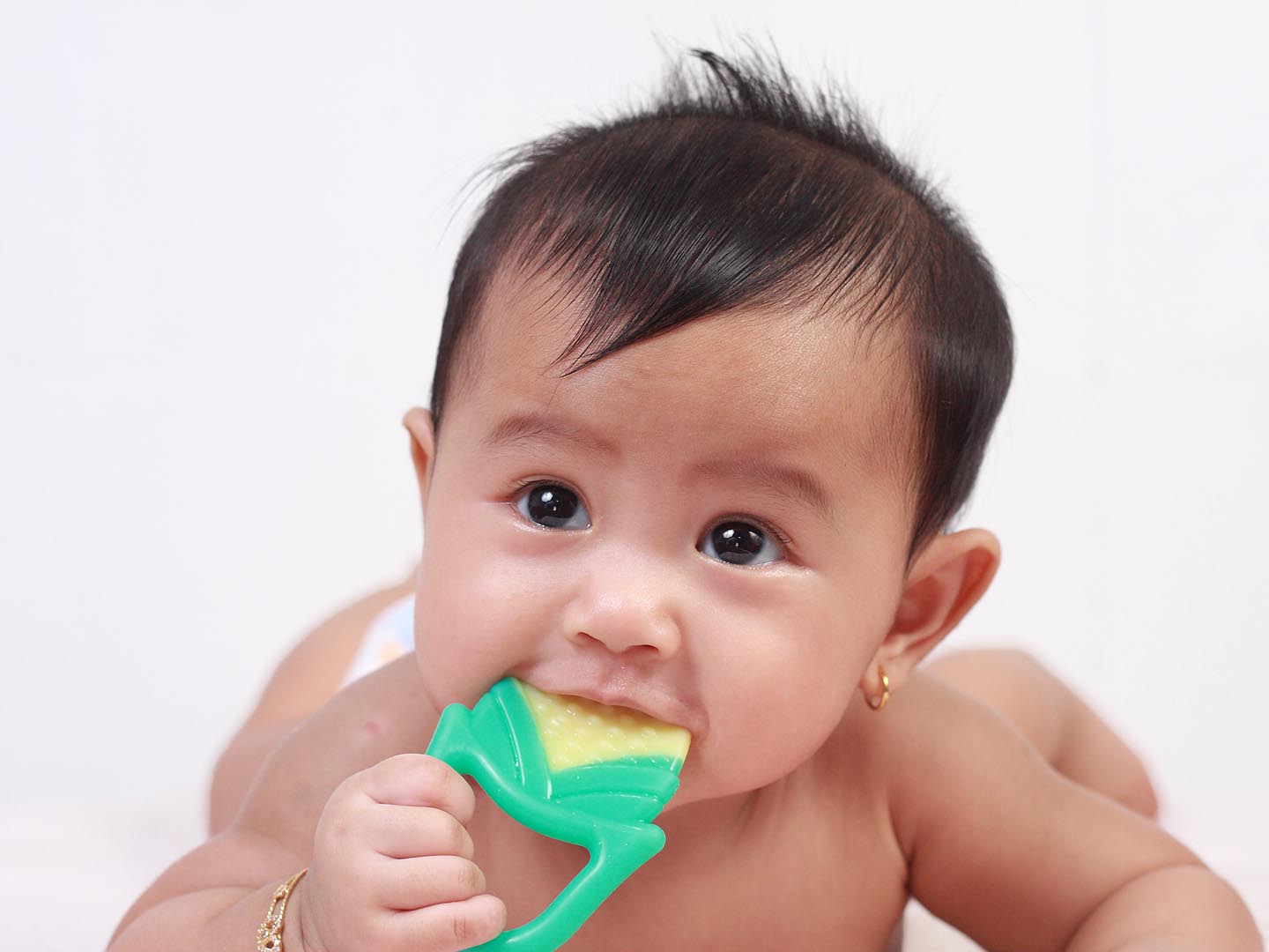 Portrait of cute little Asian baby girl lying down on bed and biting rubber toy