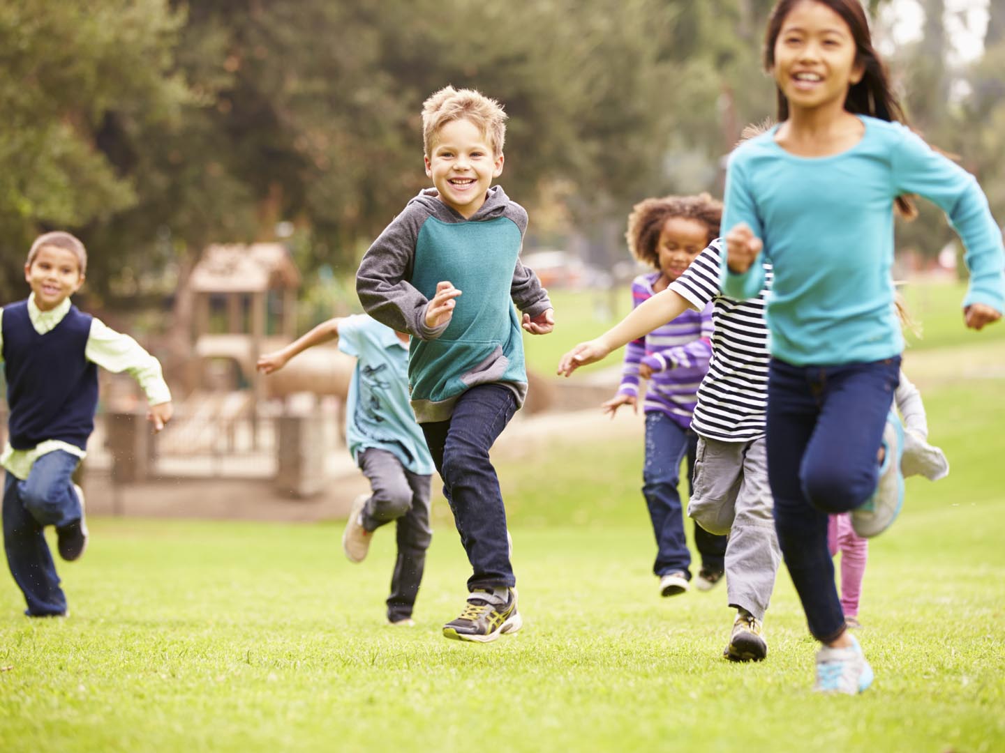 Group Of Young Children Running Towards Camera In Park Smiling To Camera