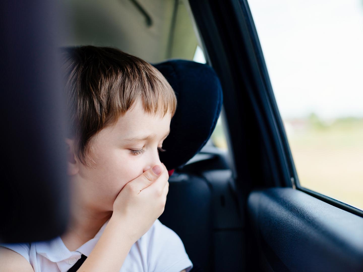 Seven years old small child in the backseat of a car sitting in children safety car seat covers his mouth with his hand - suffers from motion sickness