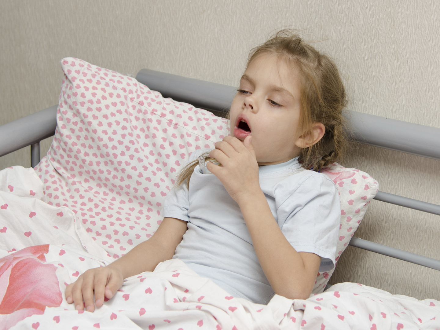 Six year old girl coughs diseased lying in bed with a thermometer on the mouse