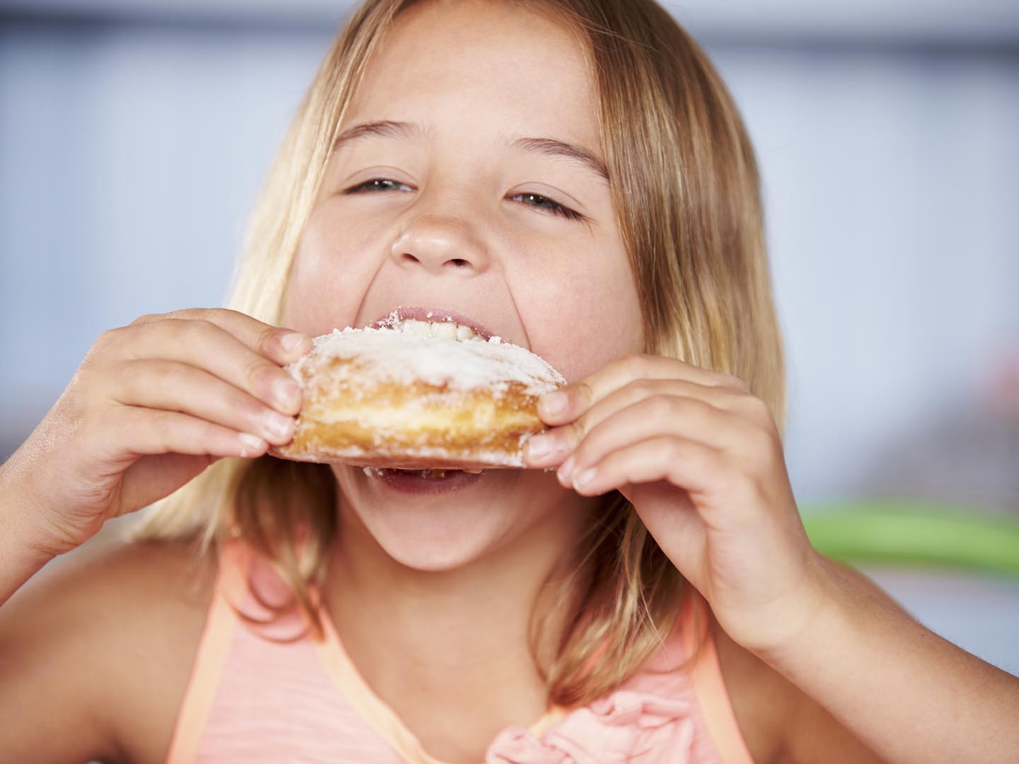 Young Girl Sitting At Table Eating Sugary Donut