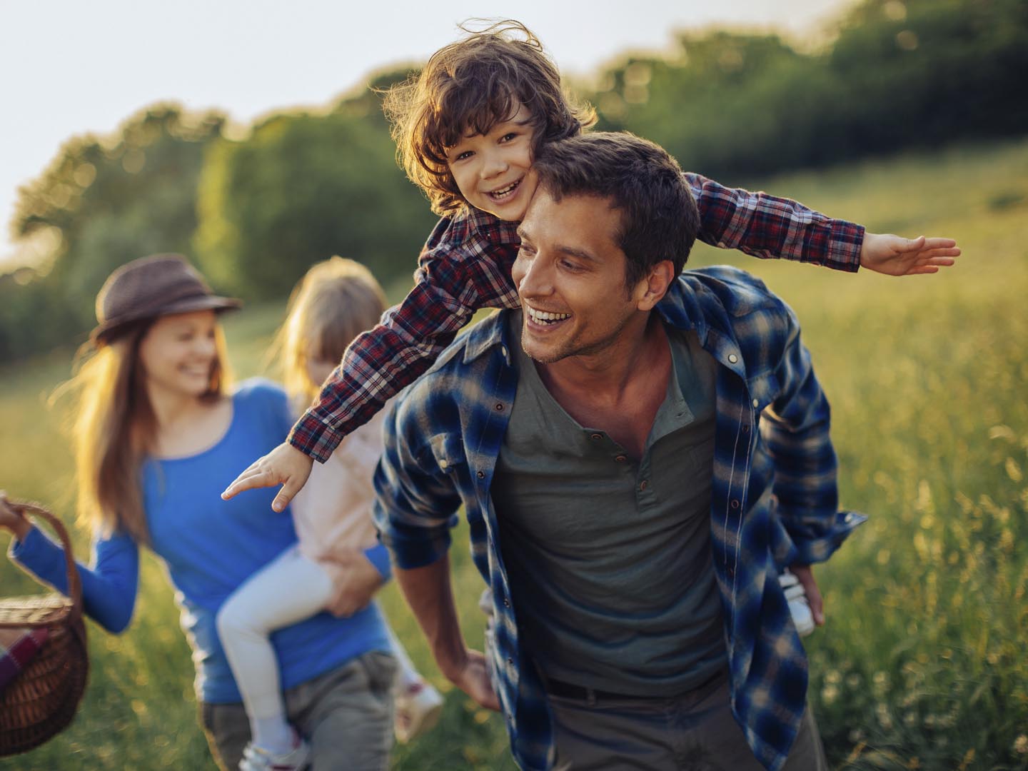 Picture of a young family going for a picnic, walking together threw high grass with the sun in their back.