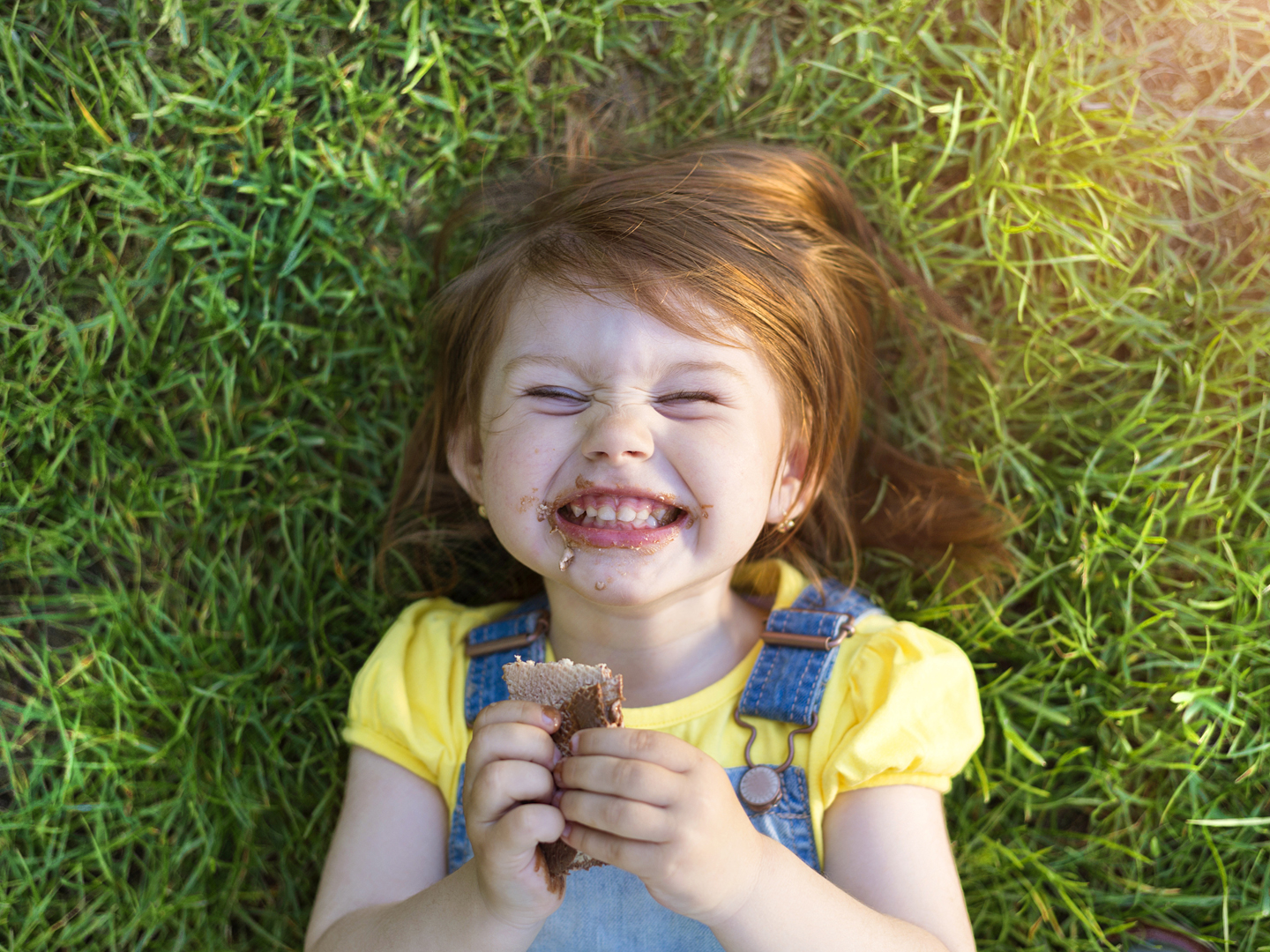 Cute little girl with chocolate face lying on a grass