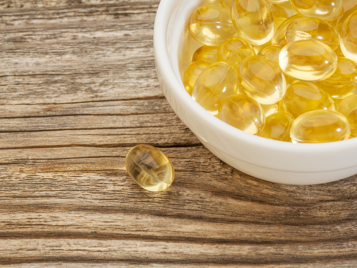fish oil capsules - a small ceramic bowl on a grained wood