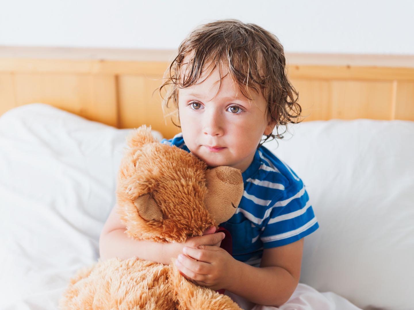 Cute toddler boy in a bed after shower, holding his teddy bear
