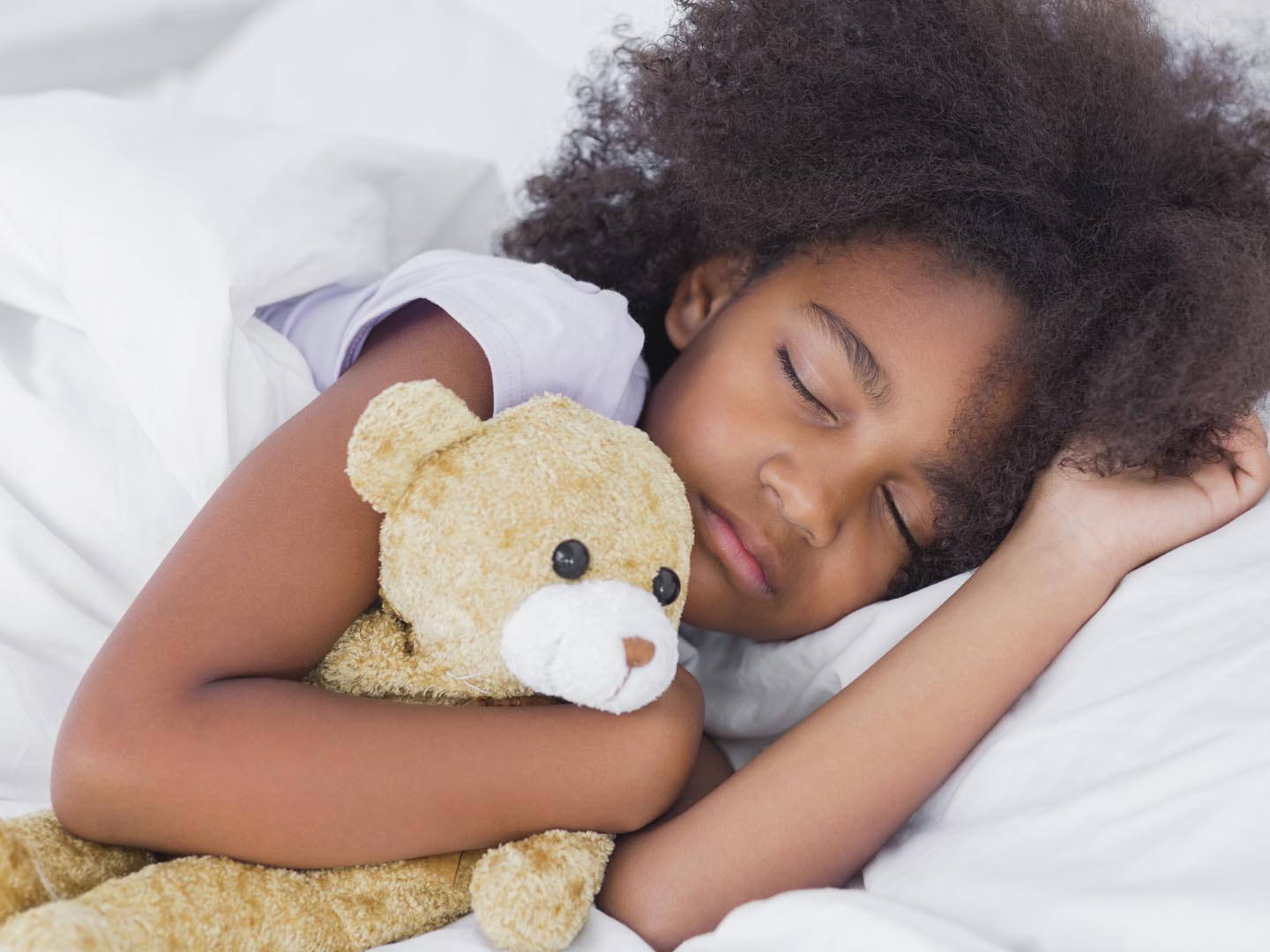 Cute little girl sleeping in bed cuddling teddy bear at home in bedroom