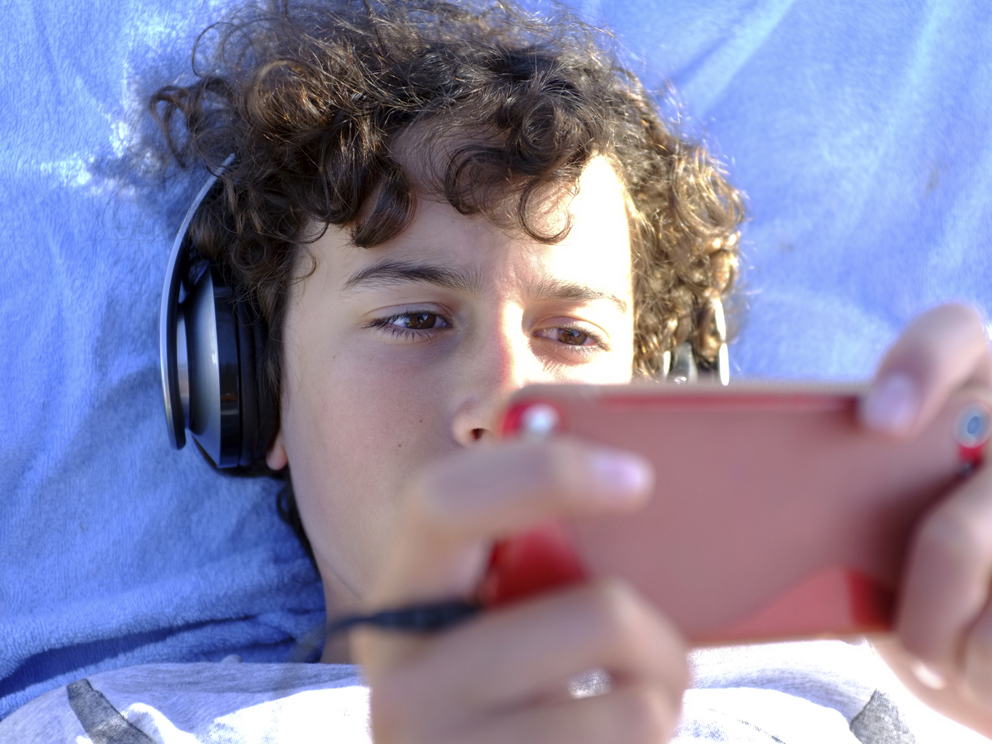 Young teen boy is listening to music with headphone and play with his gadget