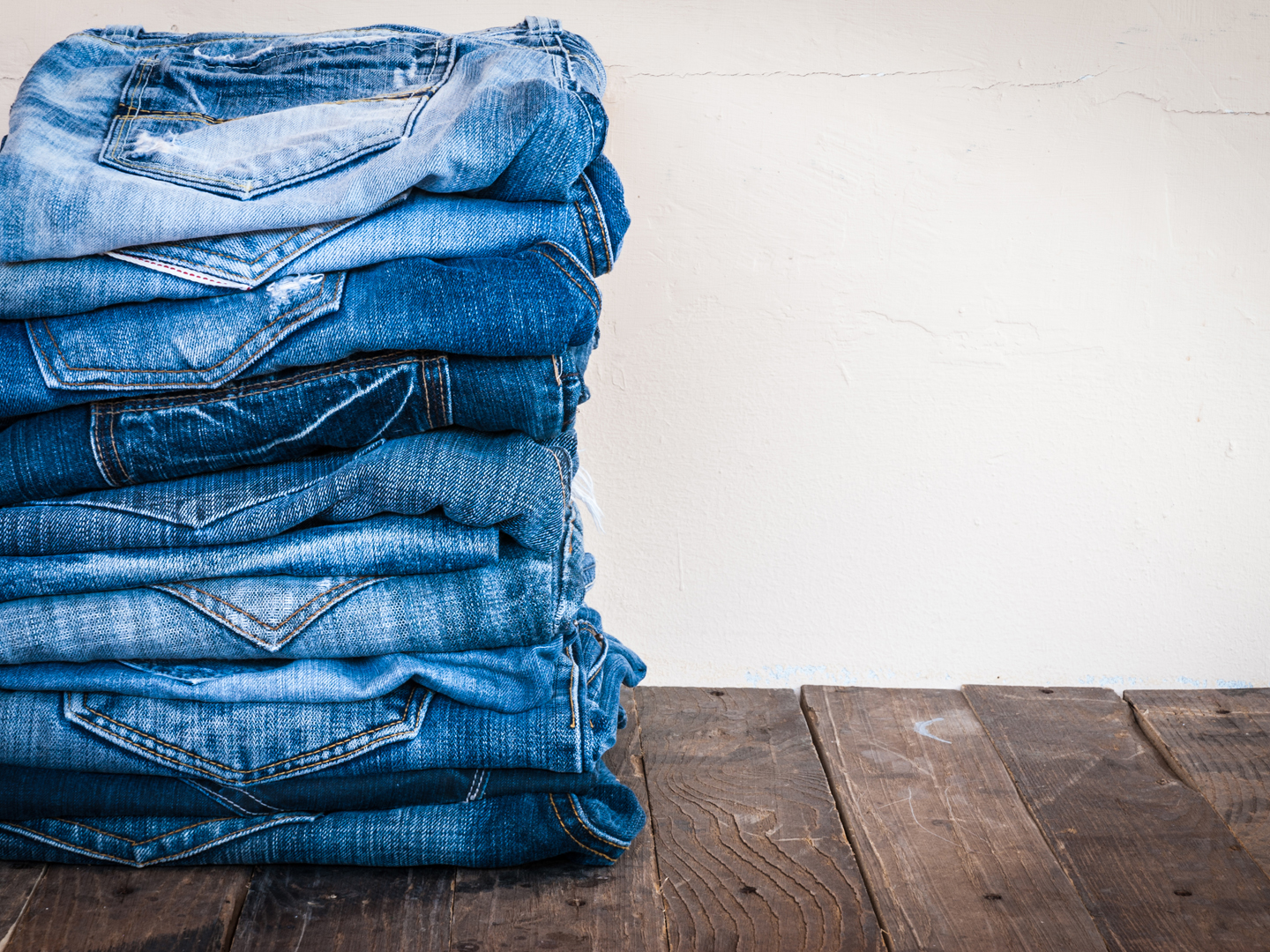 stack of various shades of blue jeans on old wood