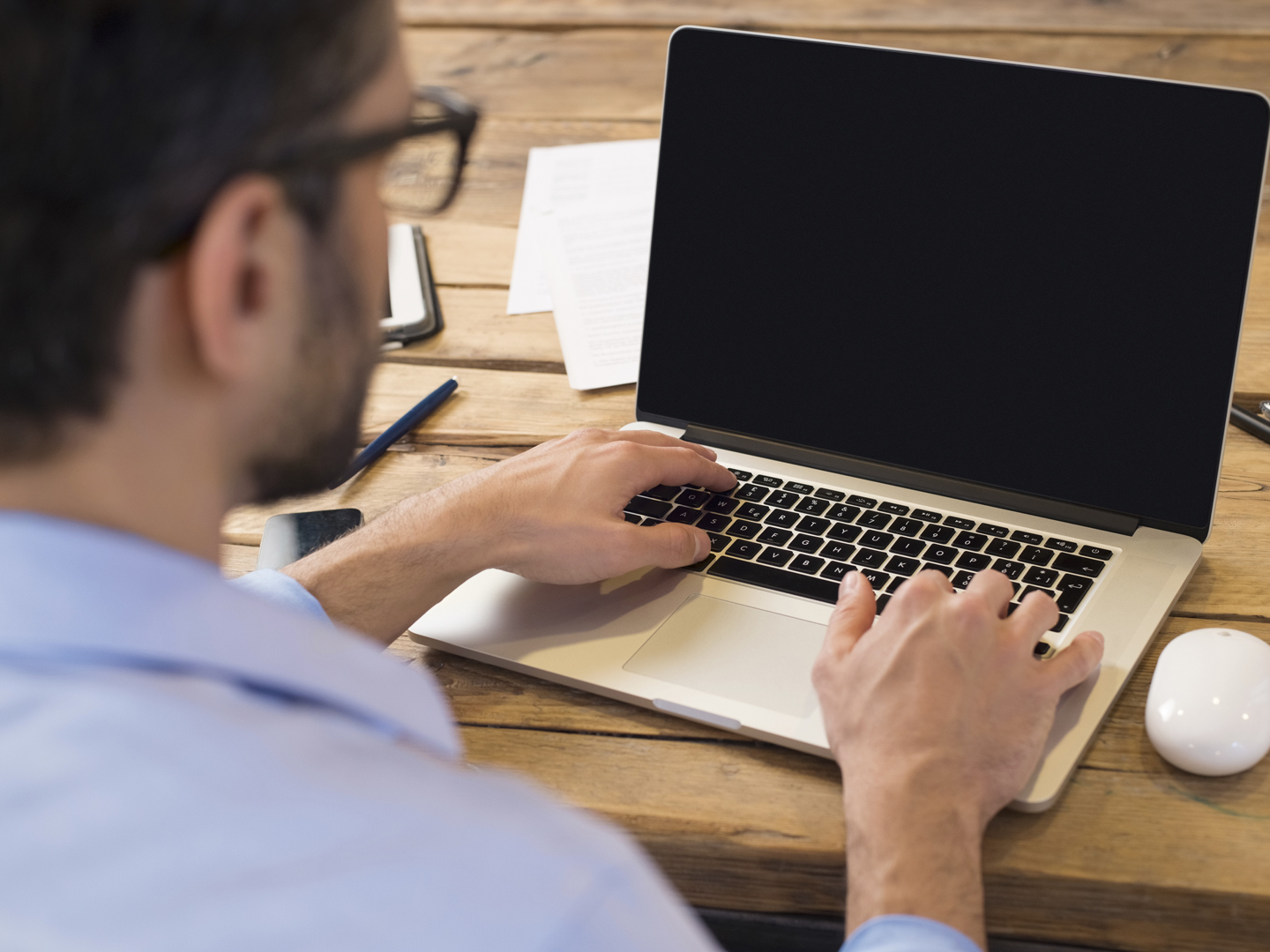 Back view of businessman sitting in front of laptop screen. Man typing on a modern laptop in an office. Young student typing on computer sitting at wooden table.