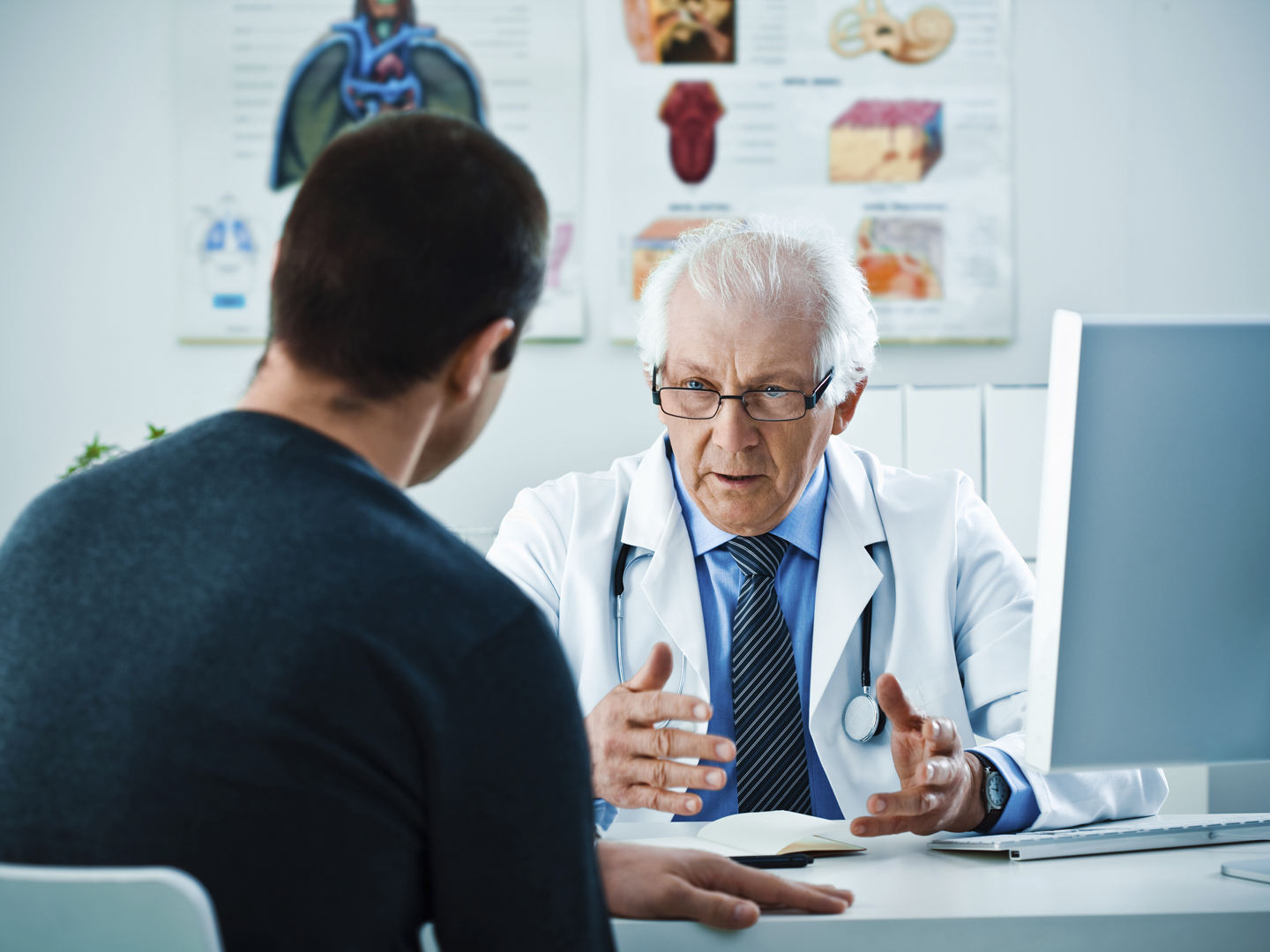 Serious senior doctor sitting at the desk in his office and talking with his patient.