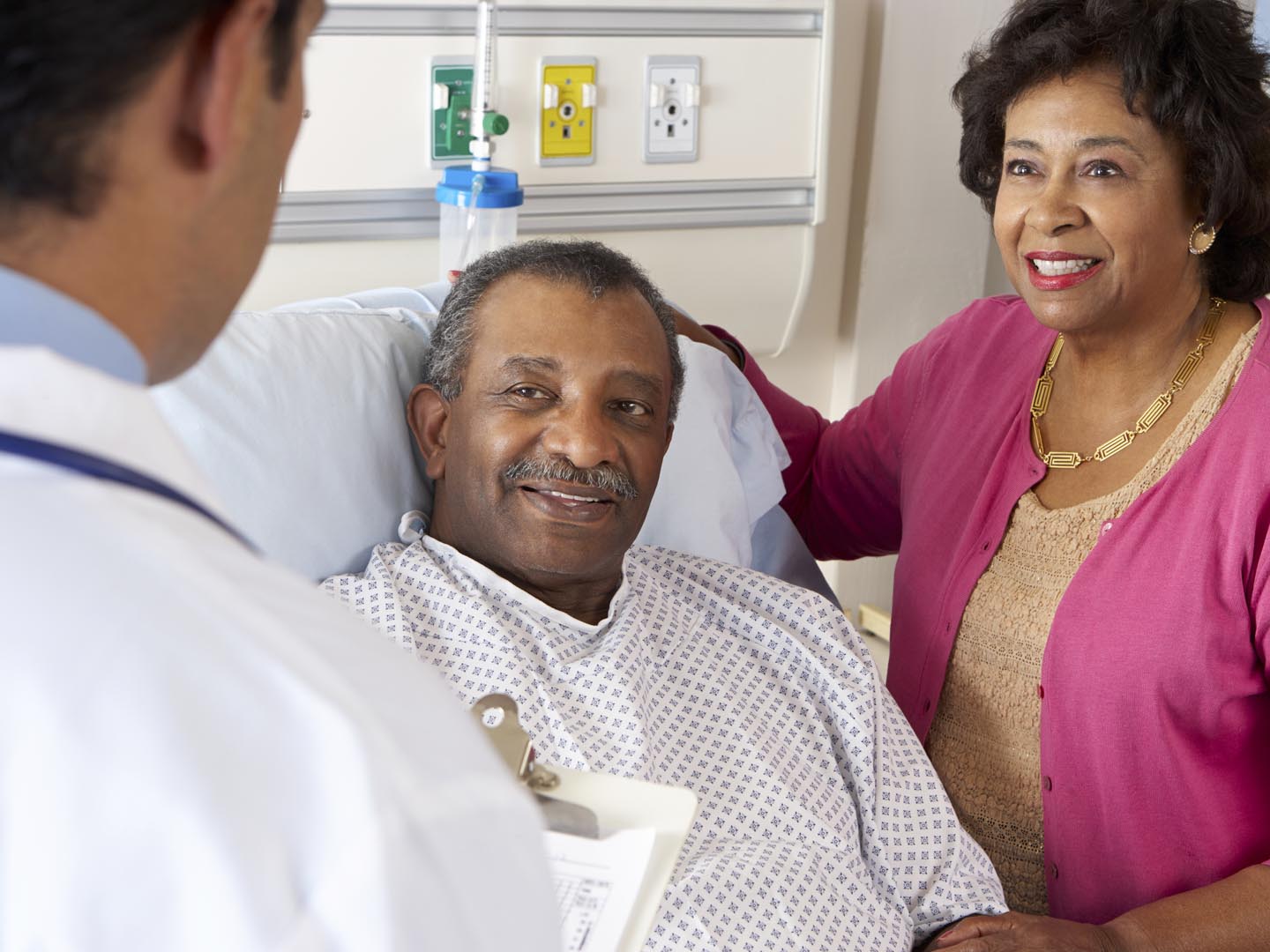 Male Doctor Talking To Senior Couple On Hospital Ward