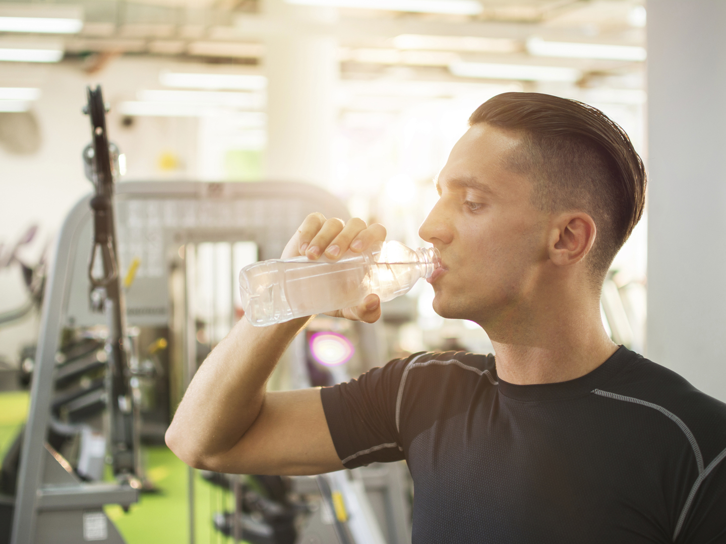 Handsome young man drinking water from a bottle and taking a break from exercising in a gym.