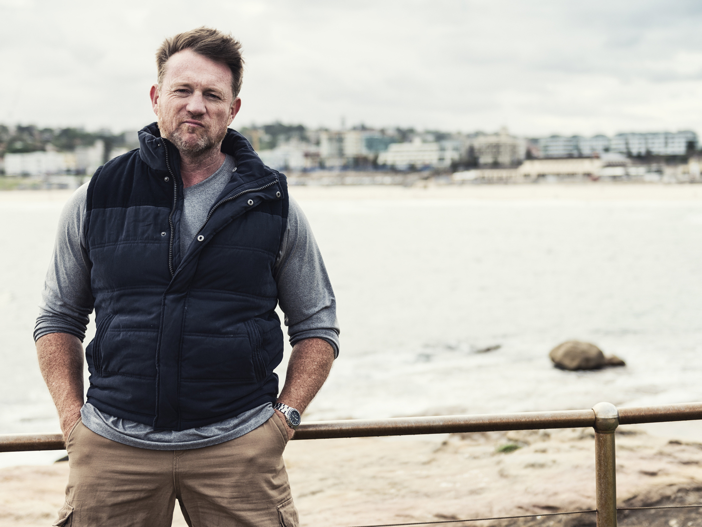 Color portrait of a mature, rugged, tough Australian man with Bondi Beach of Sydney in the background. 16x9 letterbox format with copy space on right.