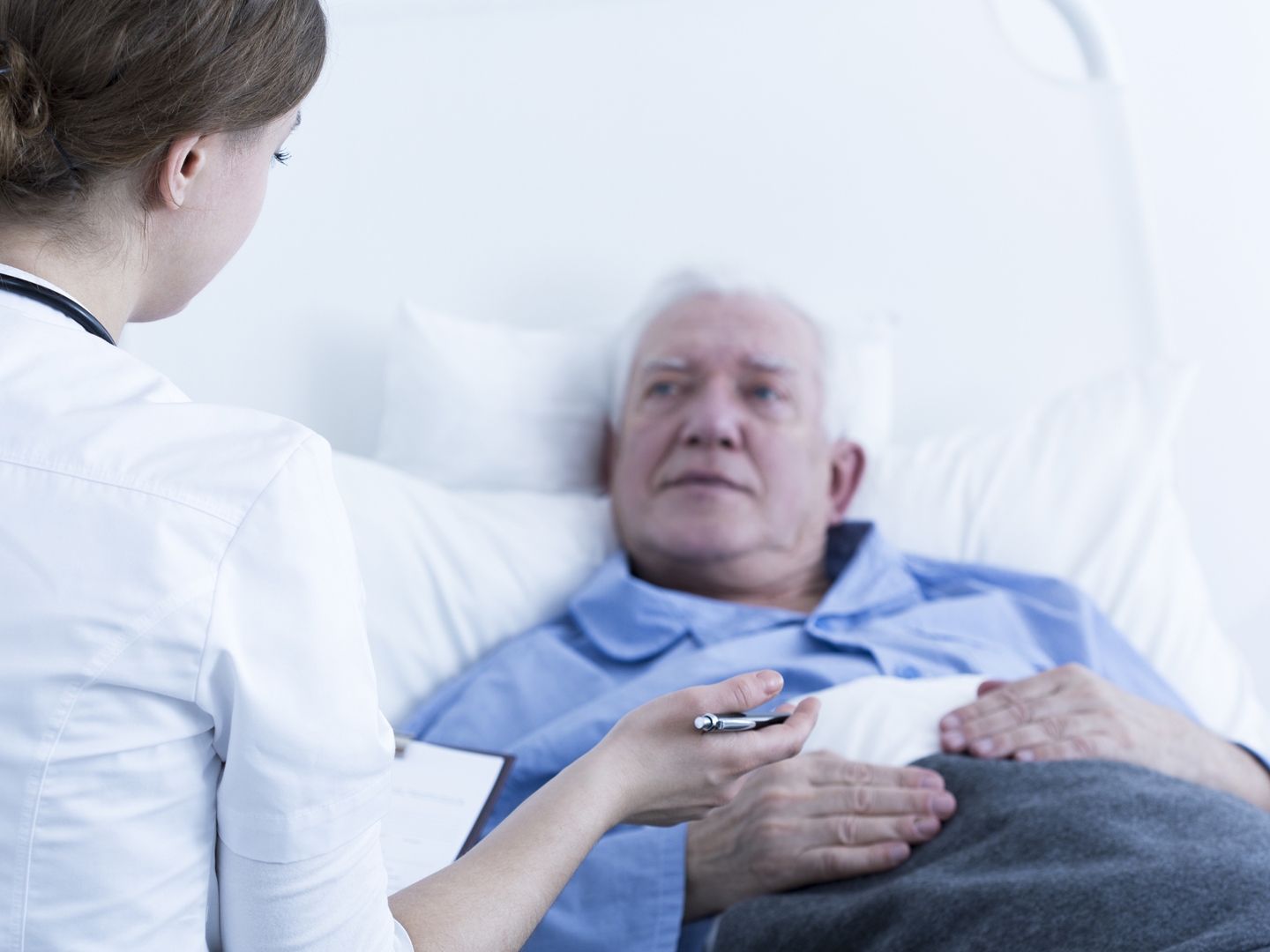 Doctor or nurse talking to elderly patient in hospital room