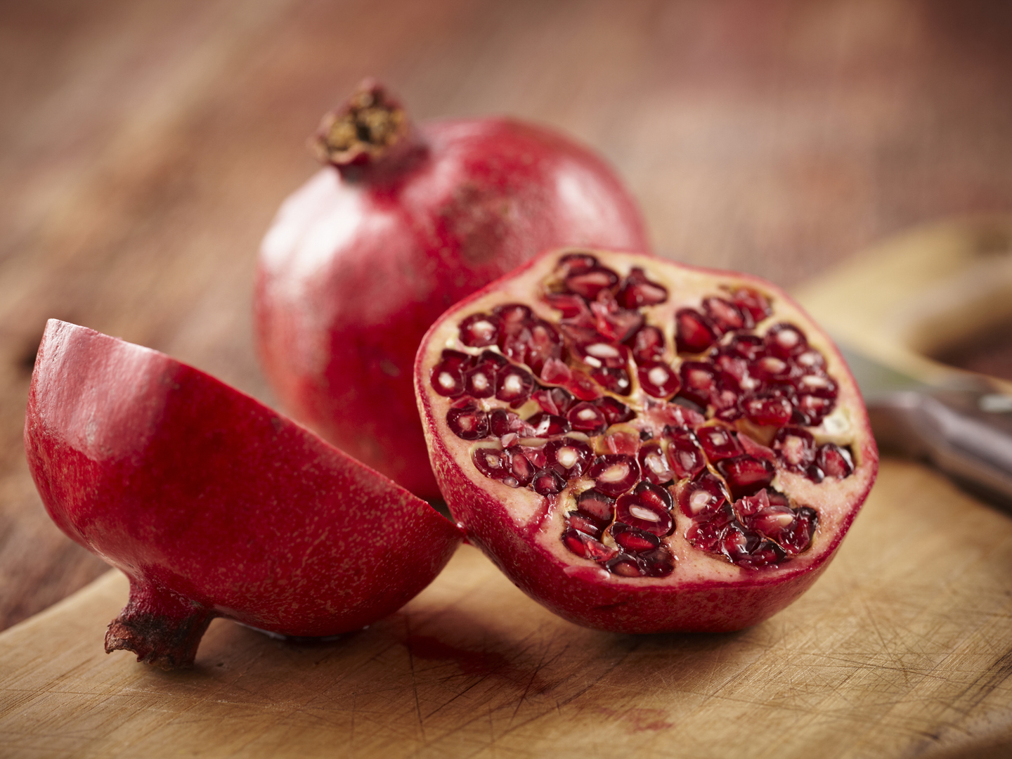 Sliced pomegranate on cutting board with knife and whole pomegranate behind.  Shot with shallow focus on sliced fruit.