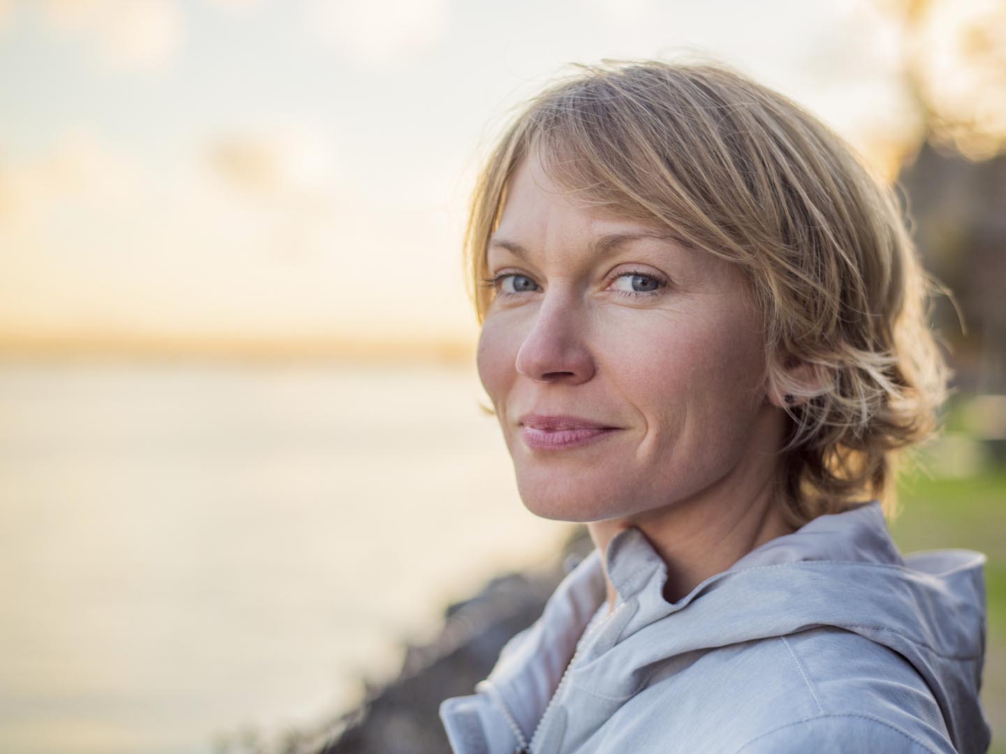 Blonde, short hair, blue eyed, mid 30&#039;s woman gives a strong contented smile as the sun sets behind her.
