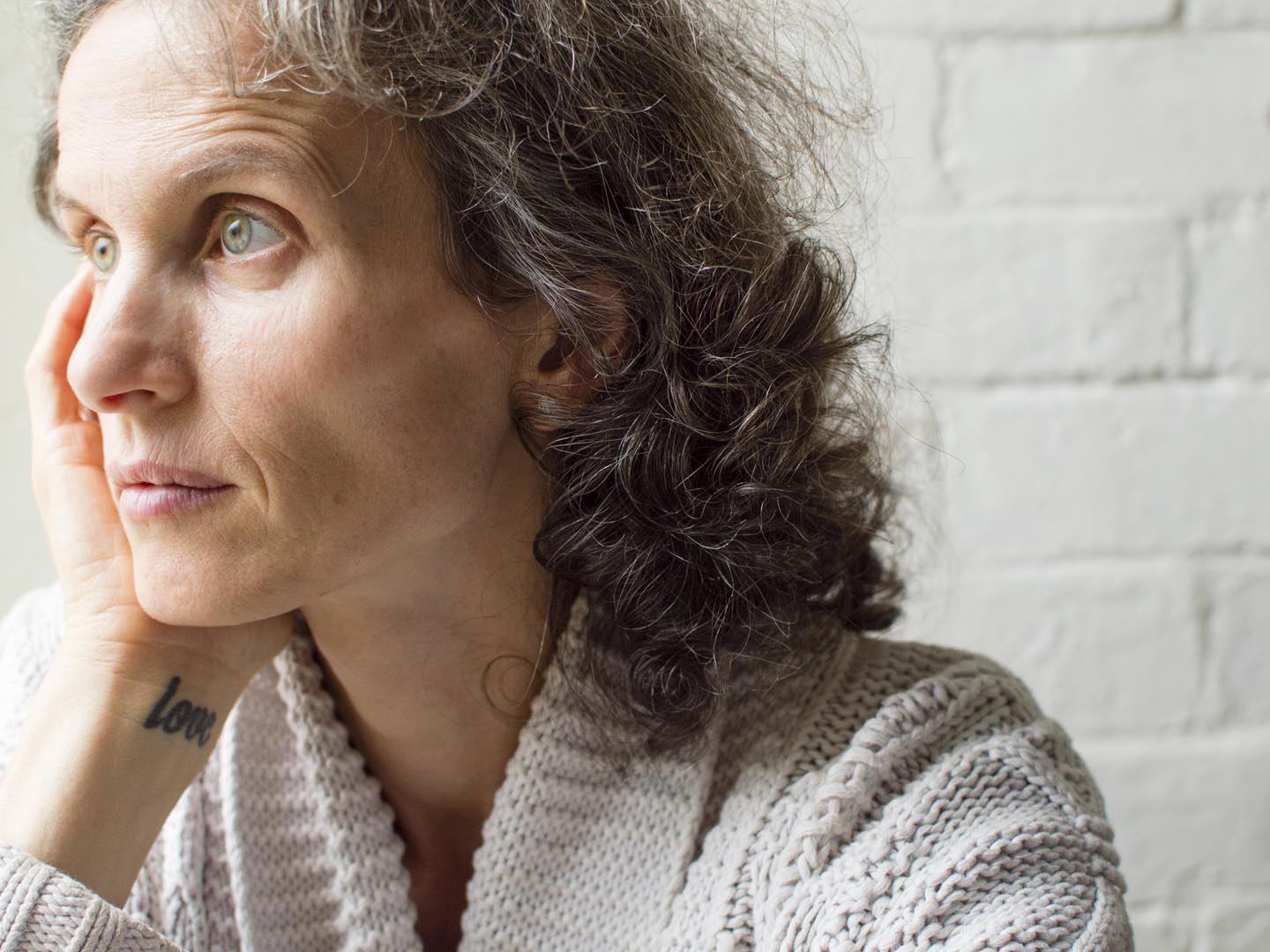 Middle aged woman in grey cardigan with hand on head, looking thoughtful (selective focus)