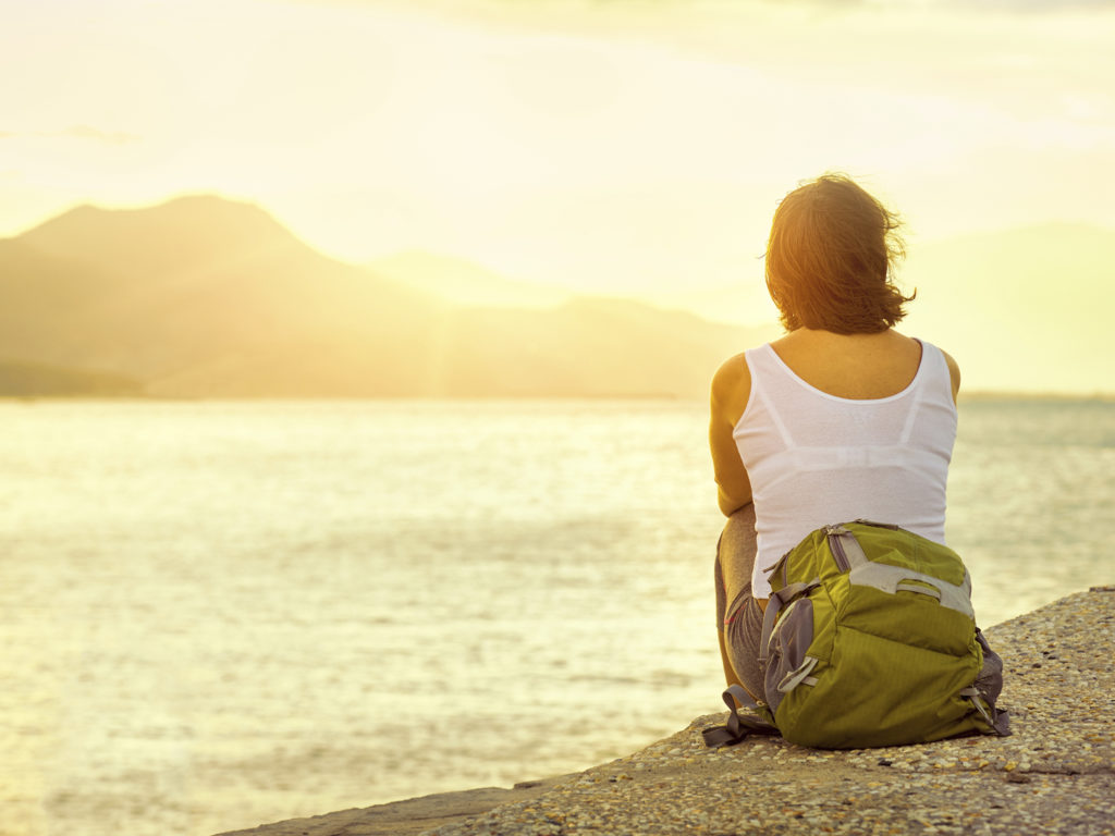 Hiker with backpack relaxing on pier .Focus on traveller. Ecotourism concept image, with happy female hiker.