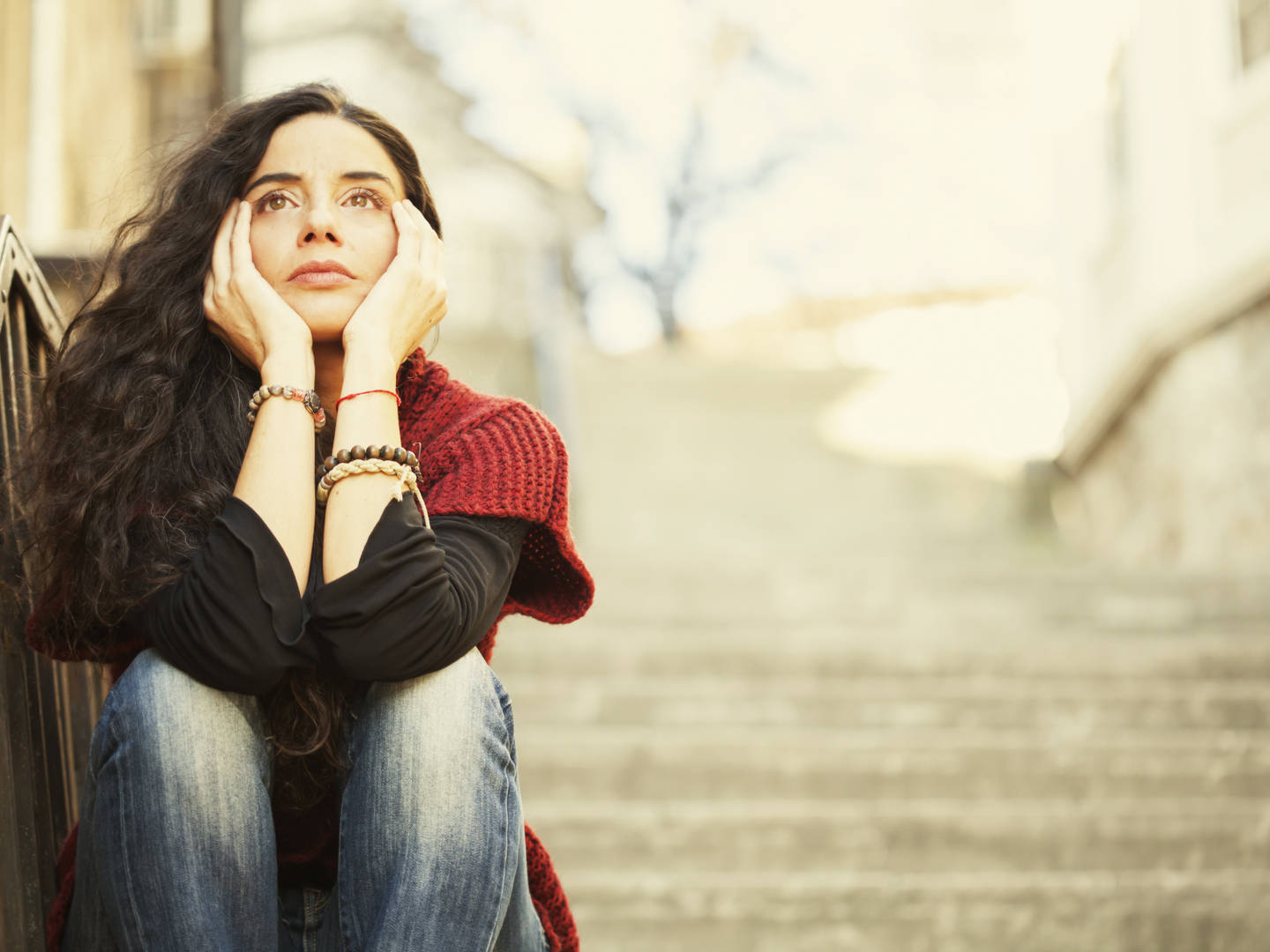 Sad young woman sitting on stairs. There are tears in her eyes