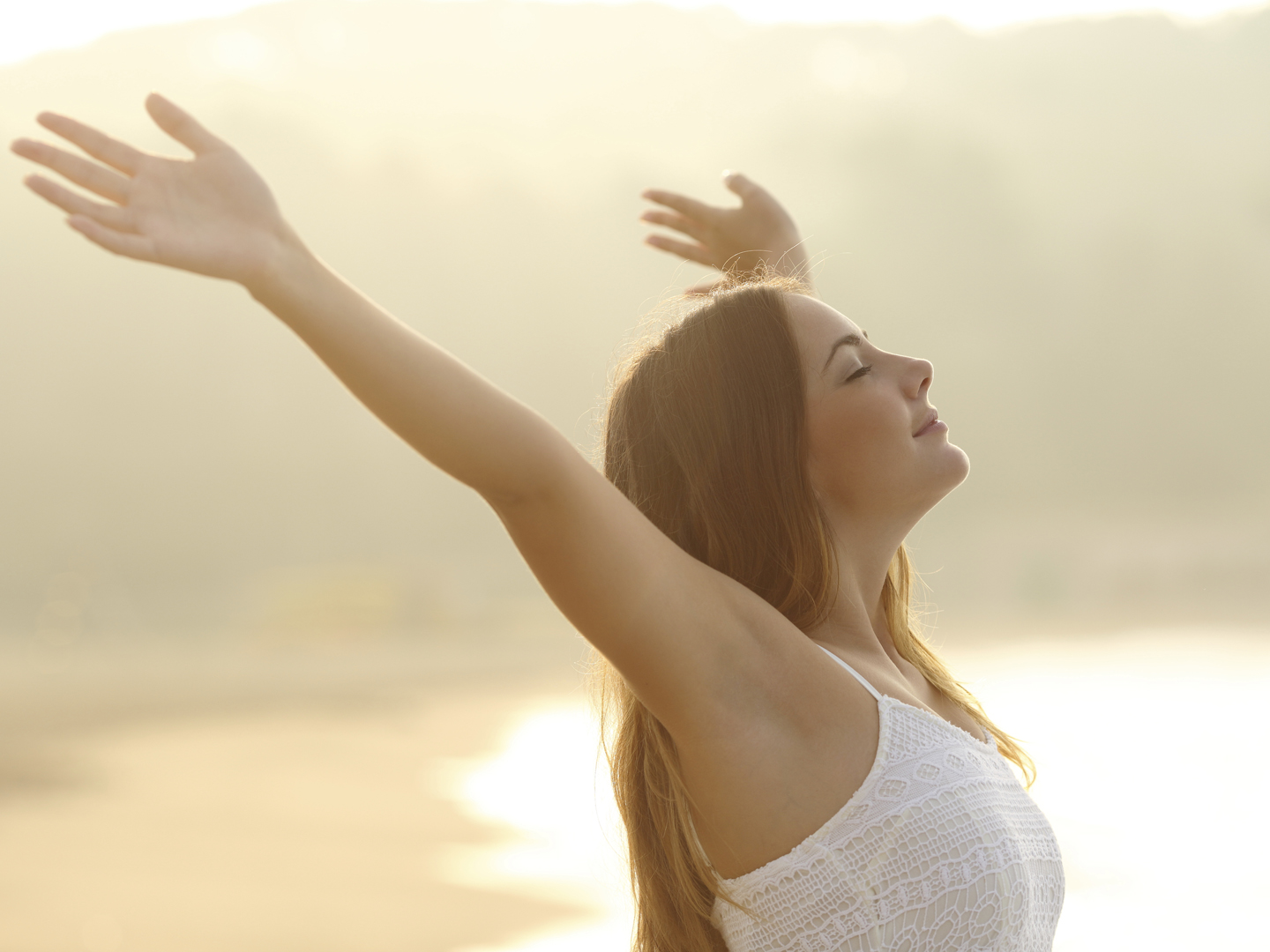 Relaxed woman breathing fresh air raising arms at sunrise with a warmth golden background