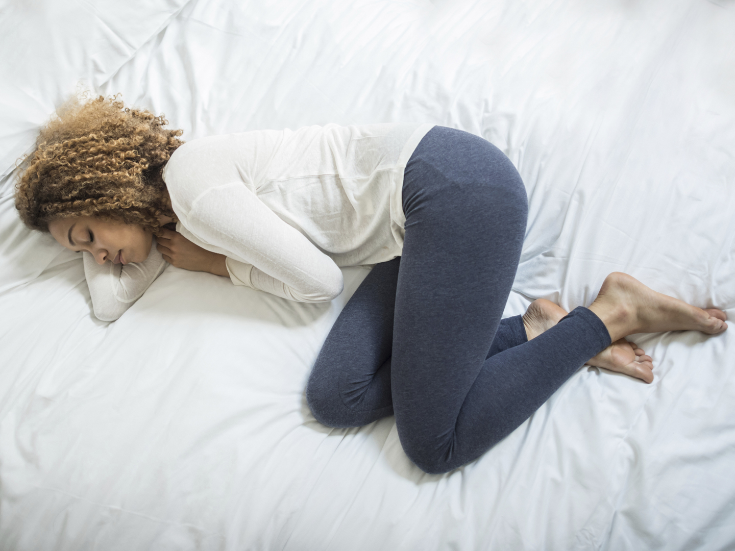 Young African American woman feeling ill and lying down on the bed