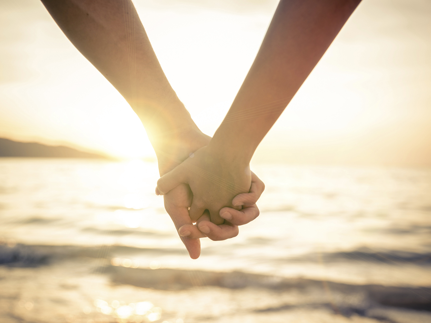 Couple of lovers holding their hands at a beautiful sunset over the ocean - Newlywed couple on a romantic vacation