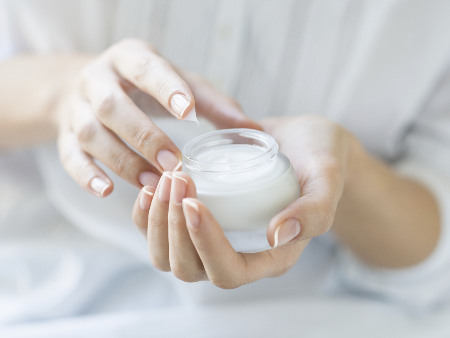 Closeup shot of hands applying moisturizer. Beauty woman holding a glass jar of skin cream. Shallow depth of field with focus on moisturizer.